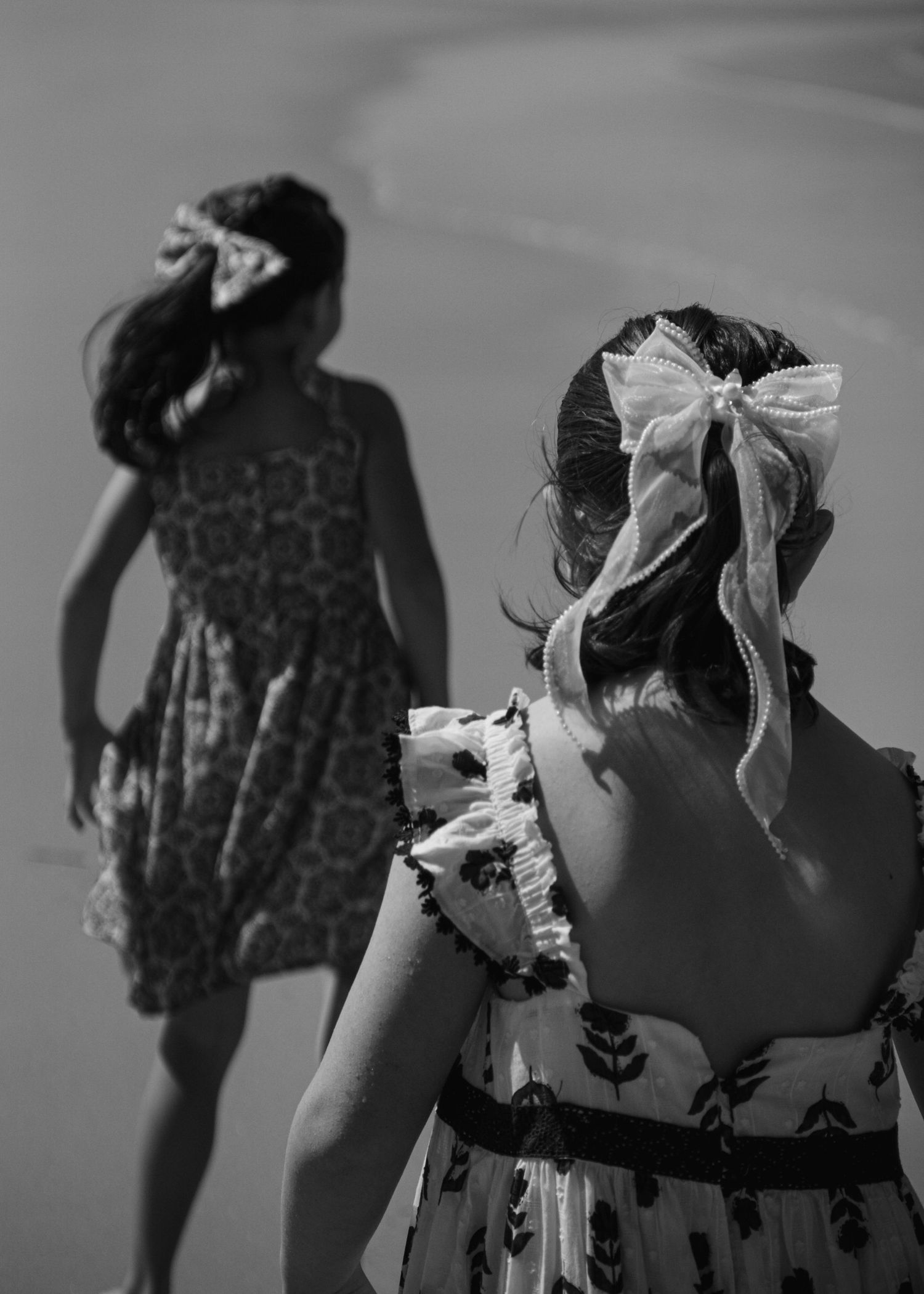 Timeless monochrome image, siblings wearing floral dresses and bows, standing together.