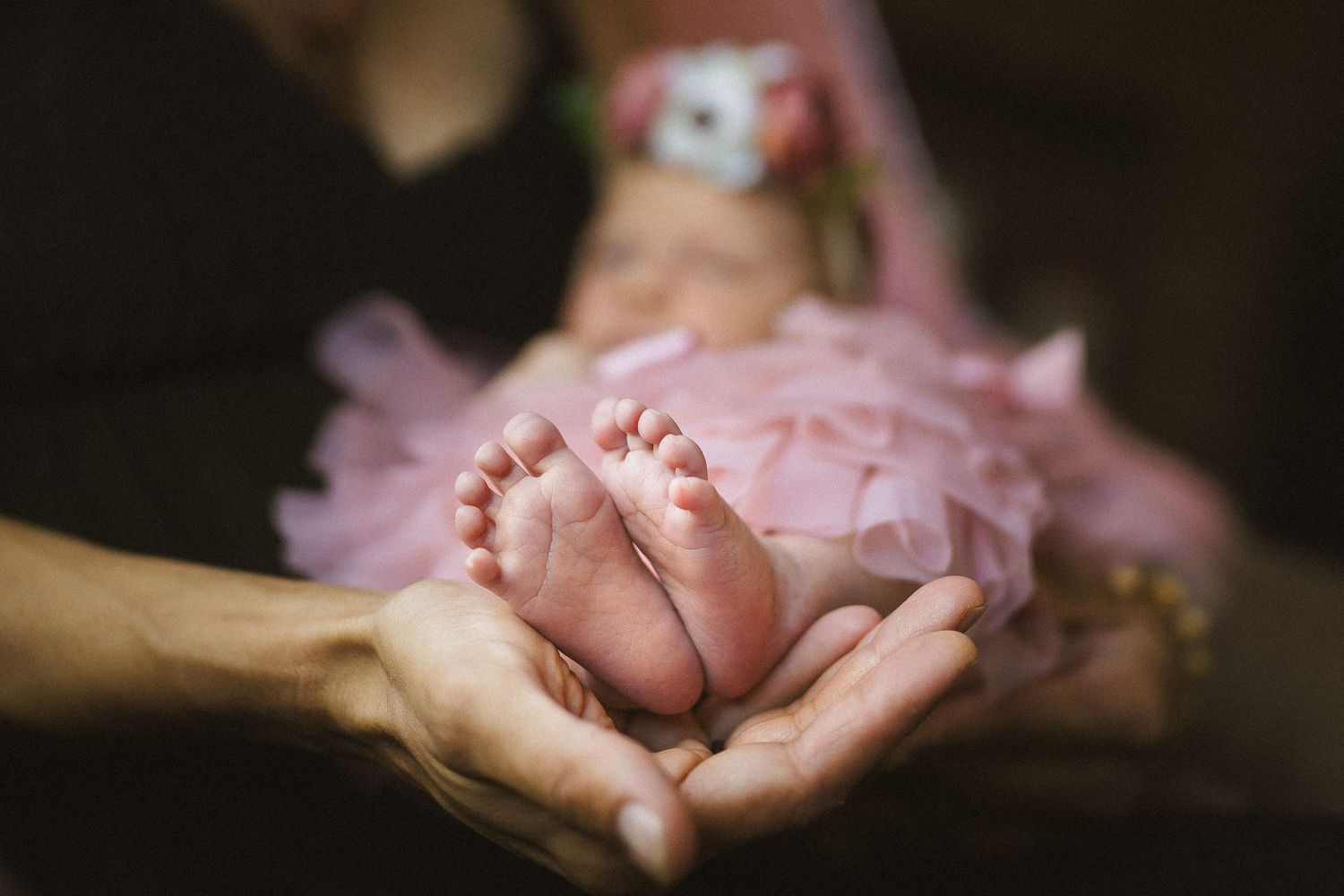 Tiny baby feet resting in hands with pink tulle dress visible.
