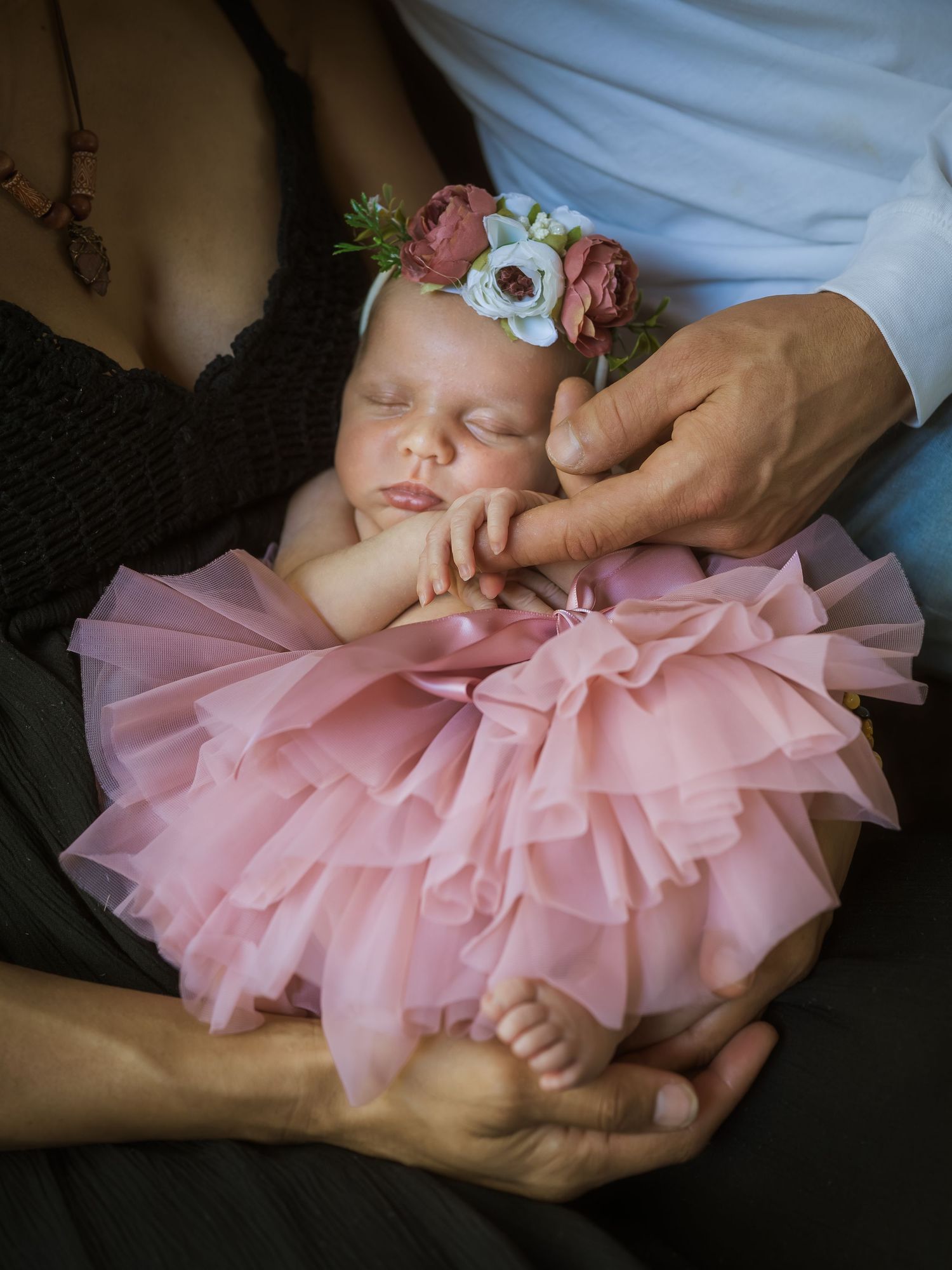 Sleeping baby in pink tulle dress and floral headband cradled in hands.
