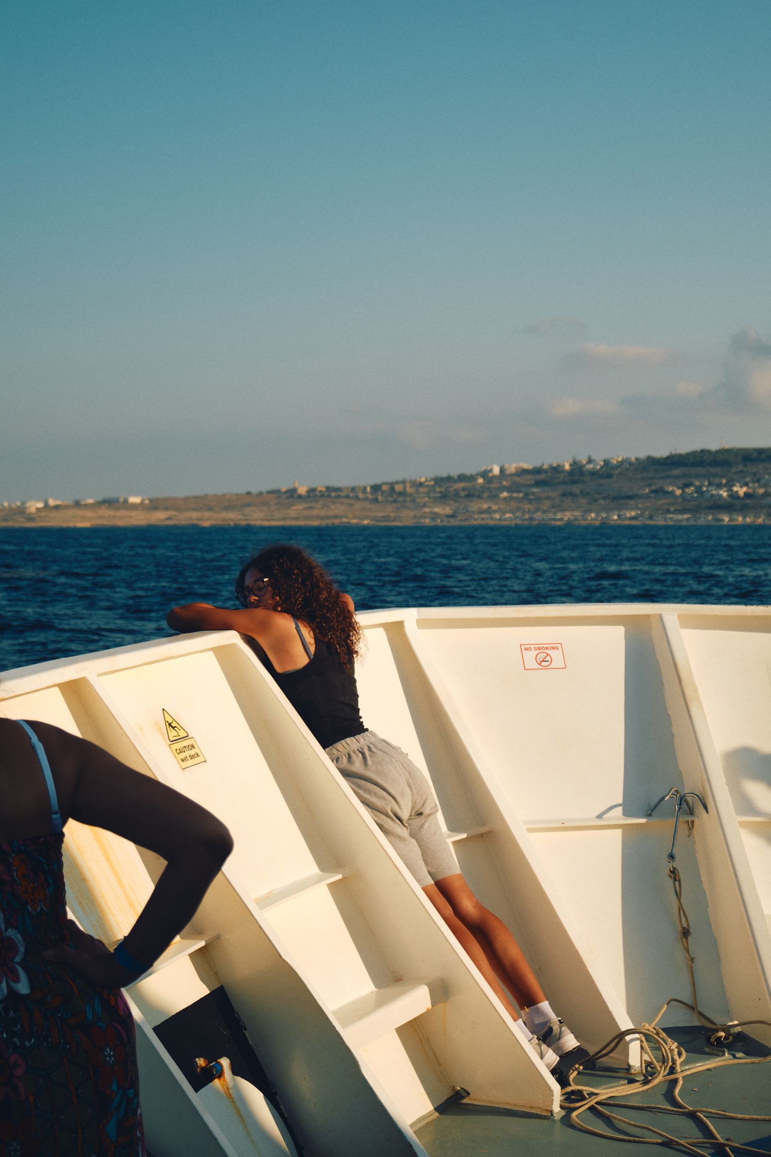 Passenger resting against white boat railing during Mediterranean sea journey.