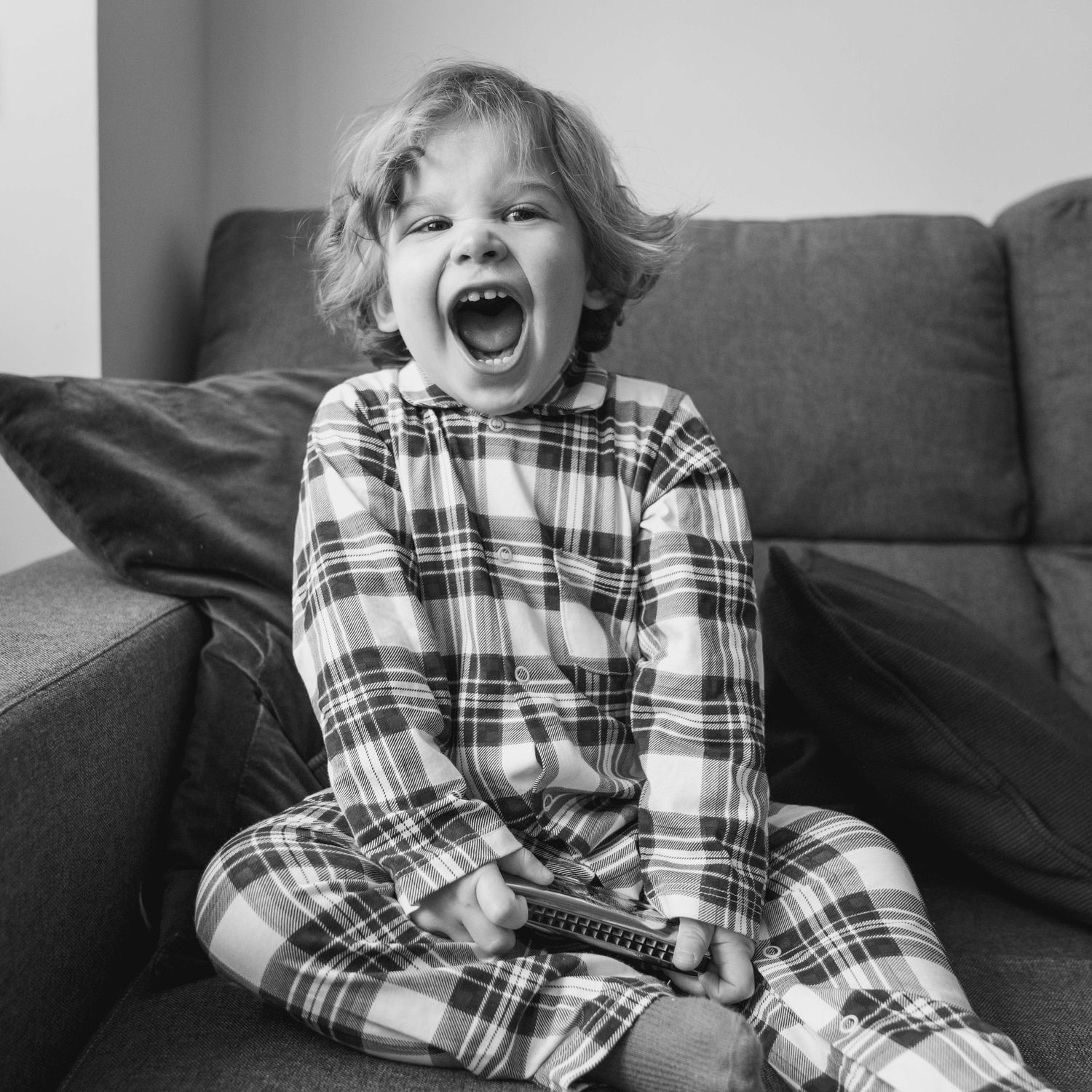 niño riendo en el sofá con pijama de cuadros durante una sesión de fotos infantil natural en casa en Madrid