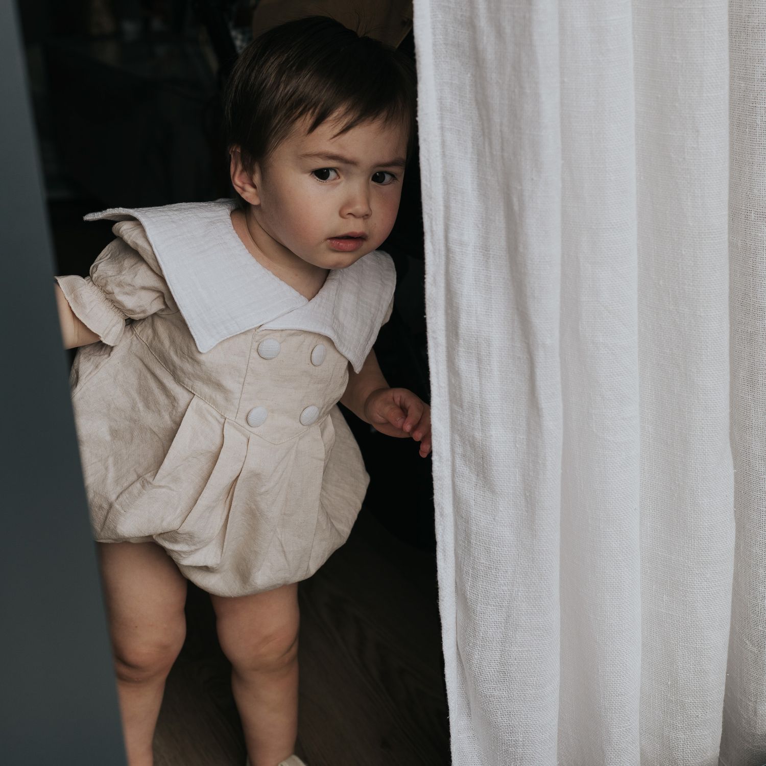 A series of moody portrait photographs showing a child in a white dress against a light curtain background.