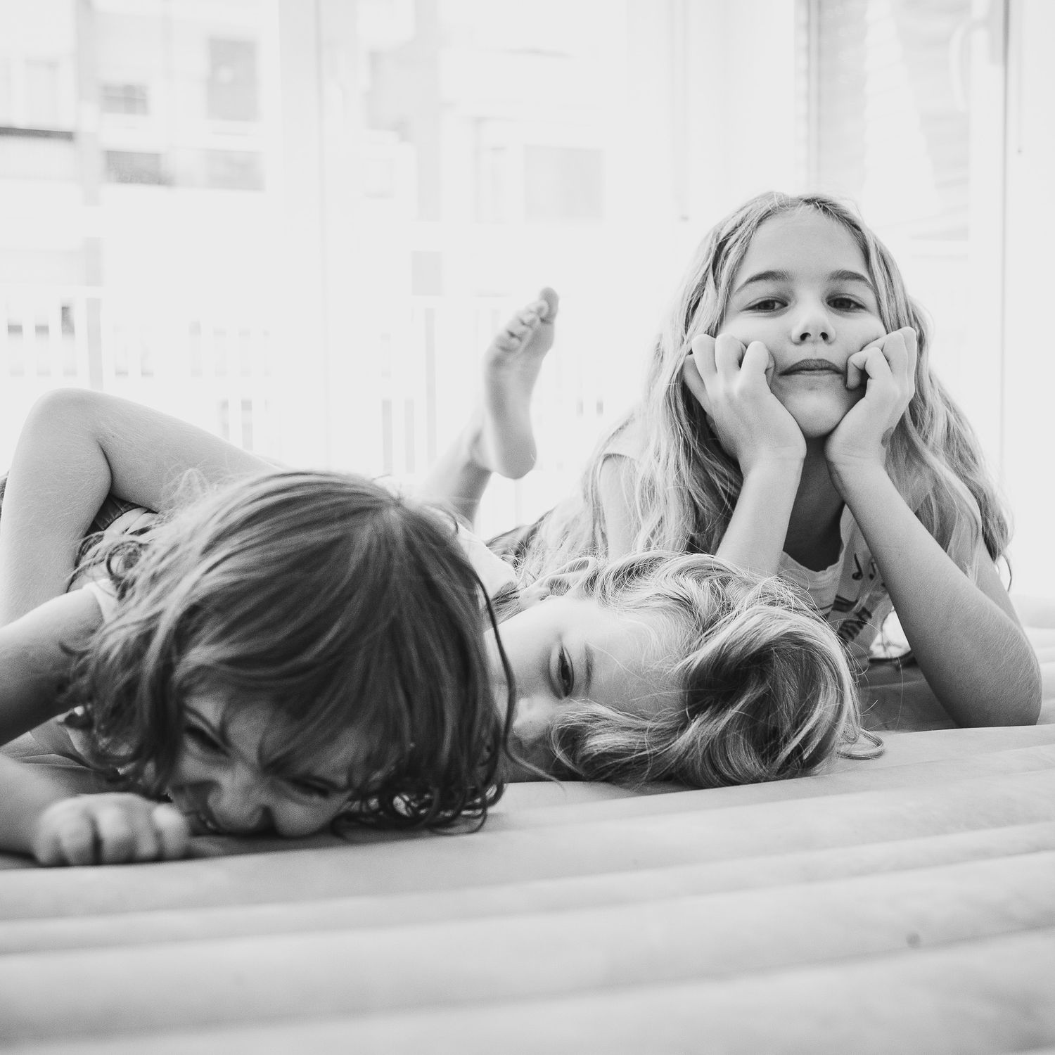 Black and white photo of children laying on floor making silly faces and playful expressions in casual setting.