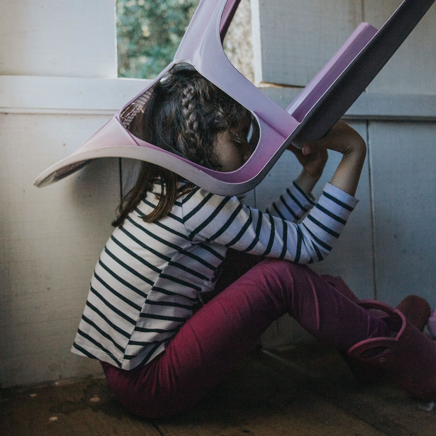 A person in a striped shirt and burgundy pants performs a dramatic dance movement against a white wall.