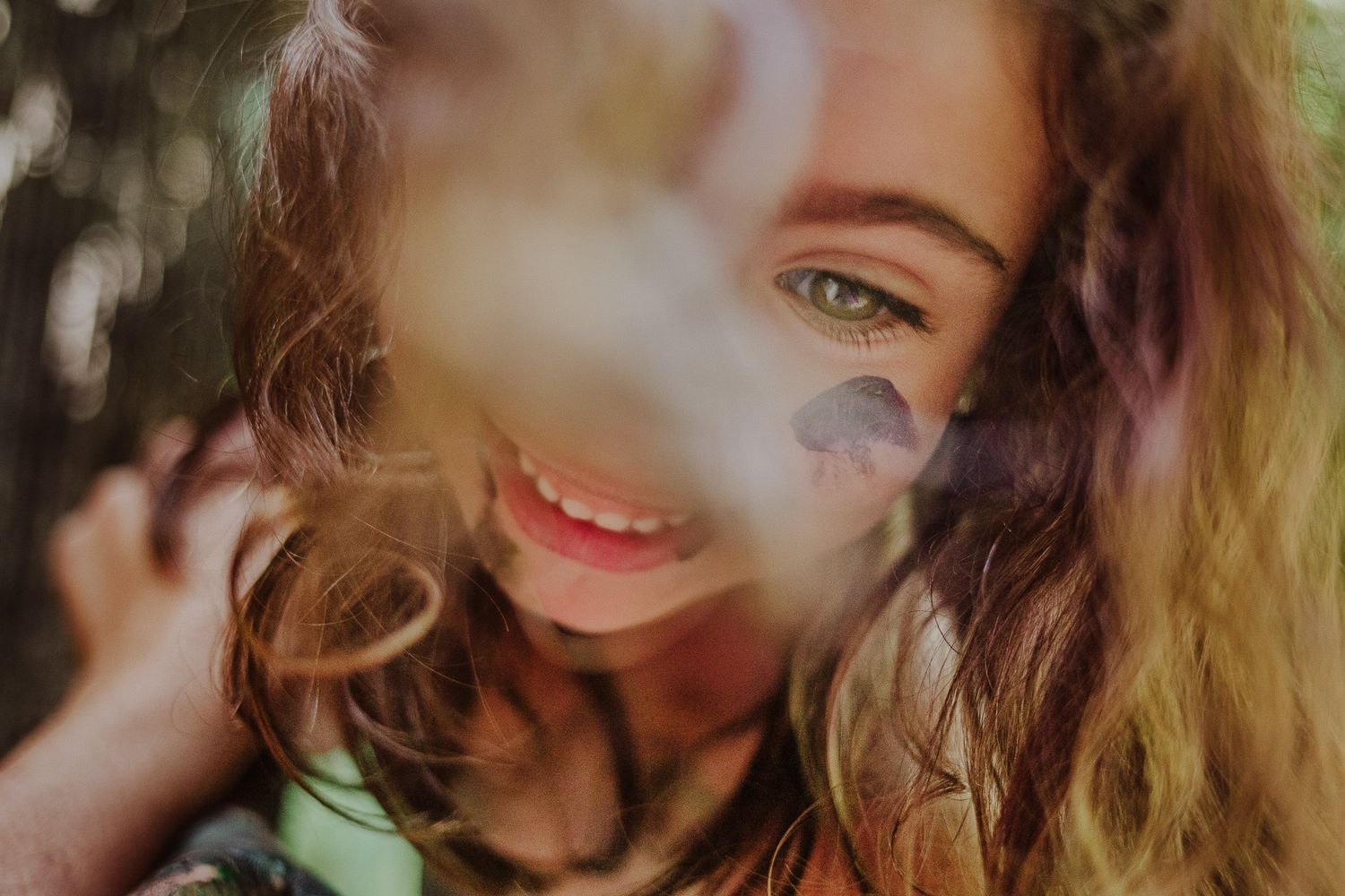 Close-up portrait of a person with long wavy hair and natural makeup smiling at the camera.