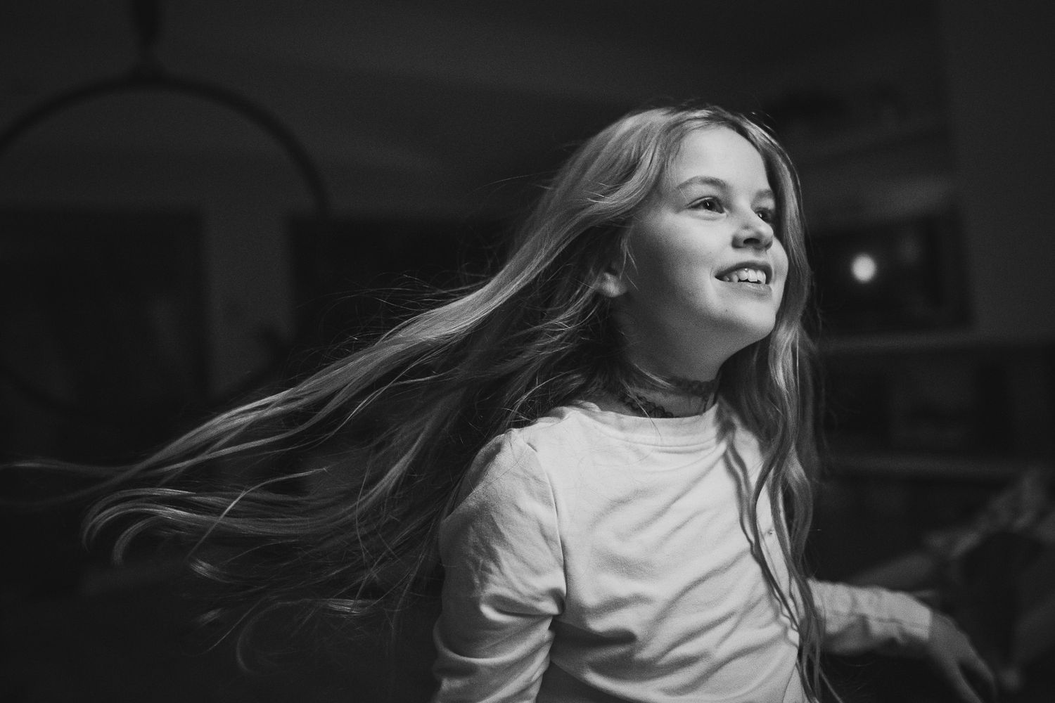Black and white photo showing someone with long flowing hair spinning and smiling in a joyful moment.