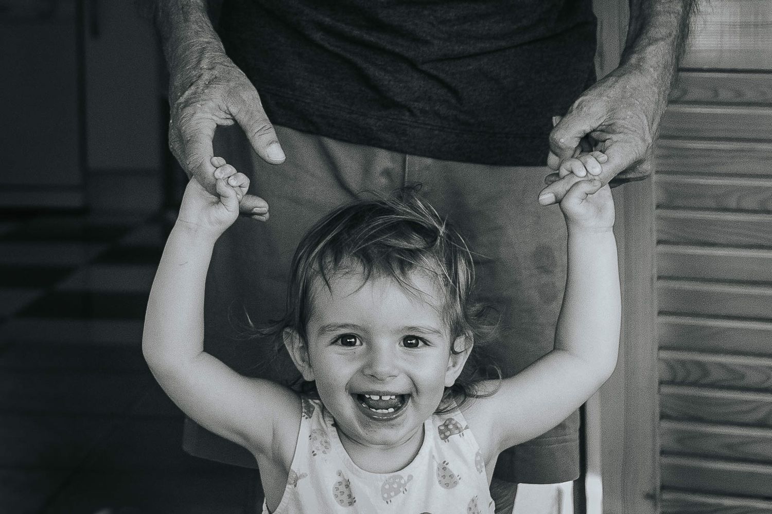 A sequence of six black and white photos shows a small child being lifted up and down while smiling and laughing.