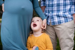 A child in a yellow sweater laughing while standing between two adults outdoors.