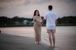 A couple stands together on a sandy beach at sunset as they share a tender moment by the water.
