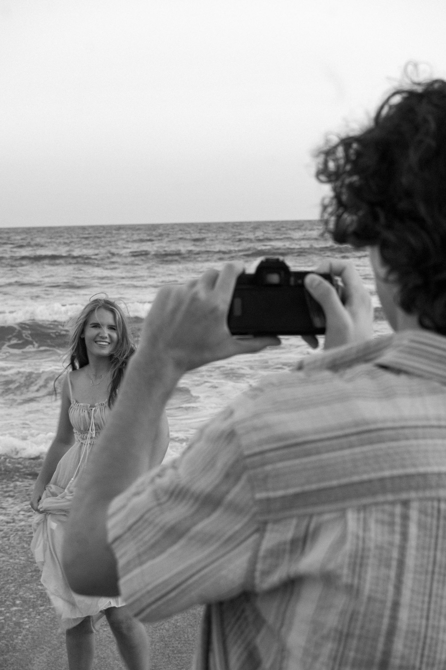 A beachside photoshoot scene with someone posing while another takes their picture against ocean waves.