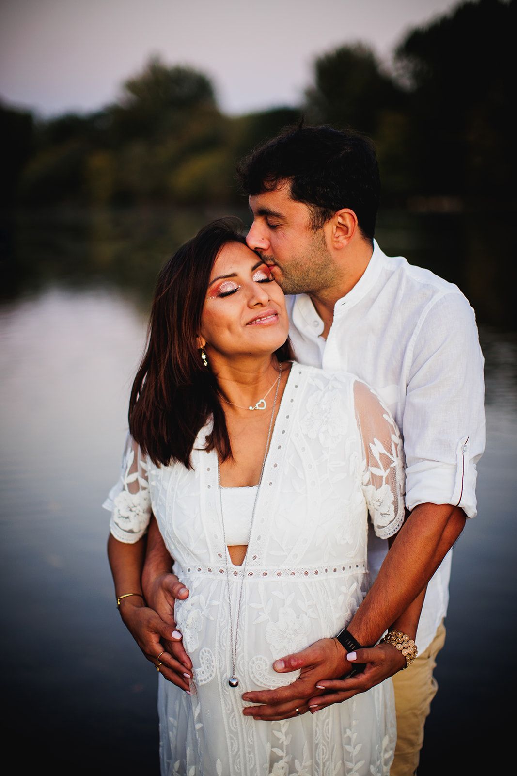Couple de futurs parents les pieds dans la rivière se faisant un calin les mains sur le ventre de la femme enceinte