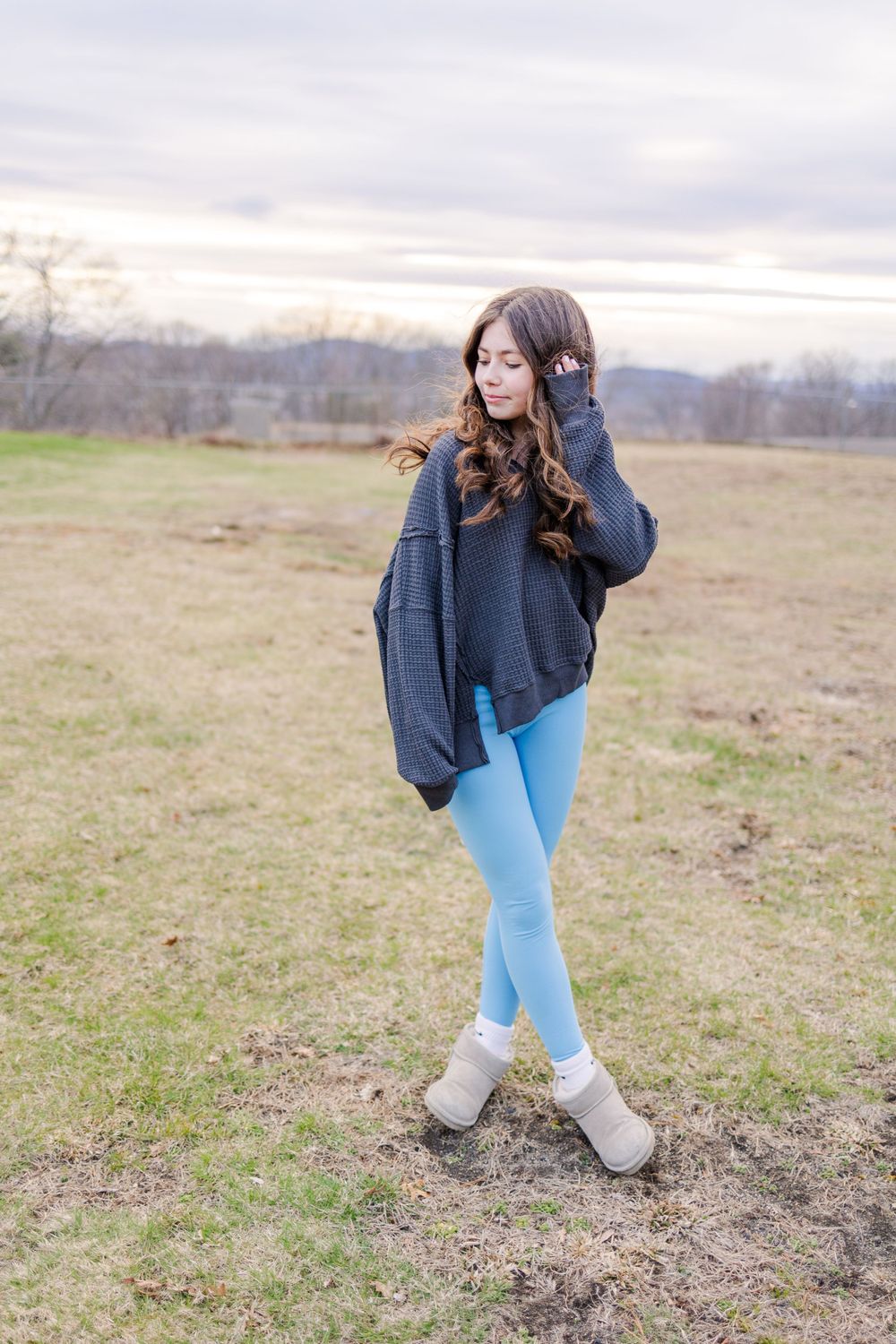 Person wearing navy sweater and blue leggings poses gracefully in a winter field.