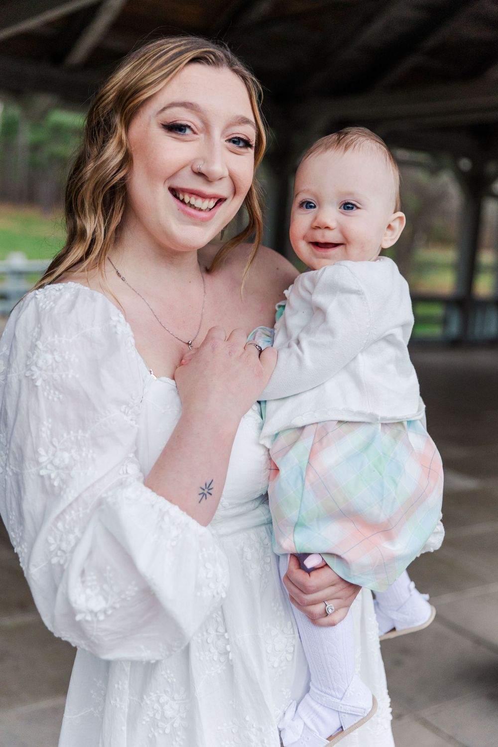 A heartwarming moment captured between a woman in a white dress and a smiling baby wearing pastel-colored clothing.