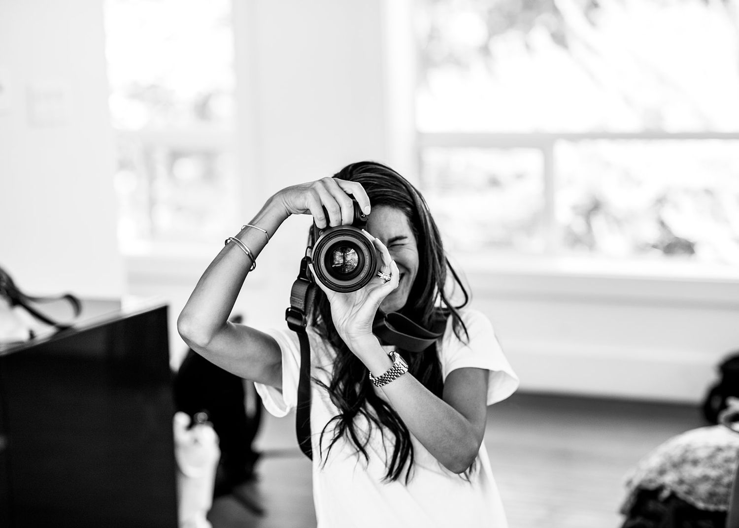 Black and white image of someone photographing with a DSLR camera near a bright window.