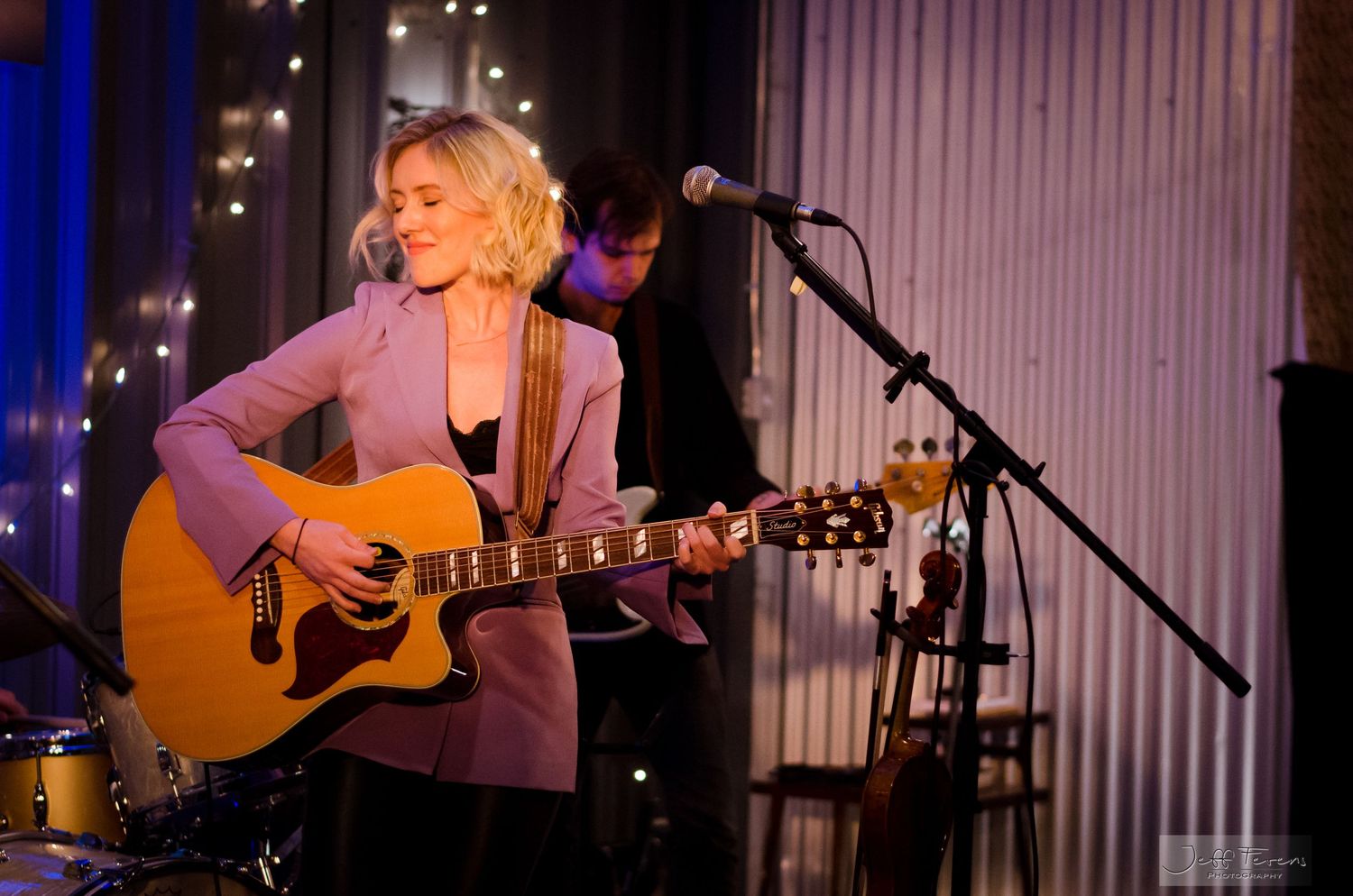 Americana female singer playing guitar on indoor stage.