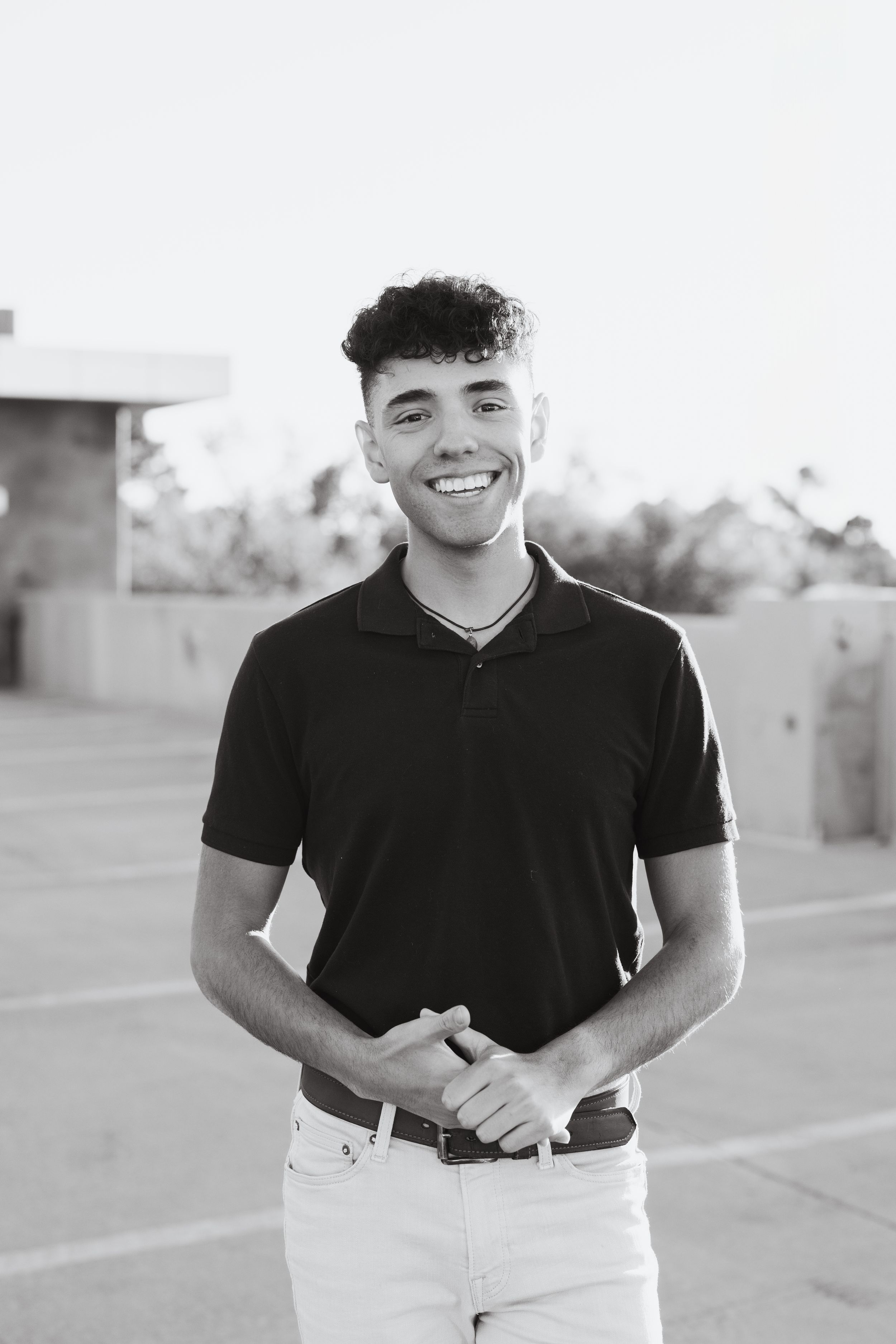 Portrait of a person in a black polo shirt smiling warmly against a bright outdoor background.