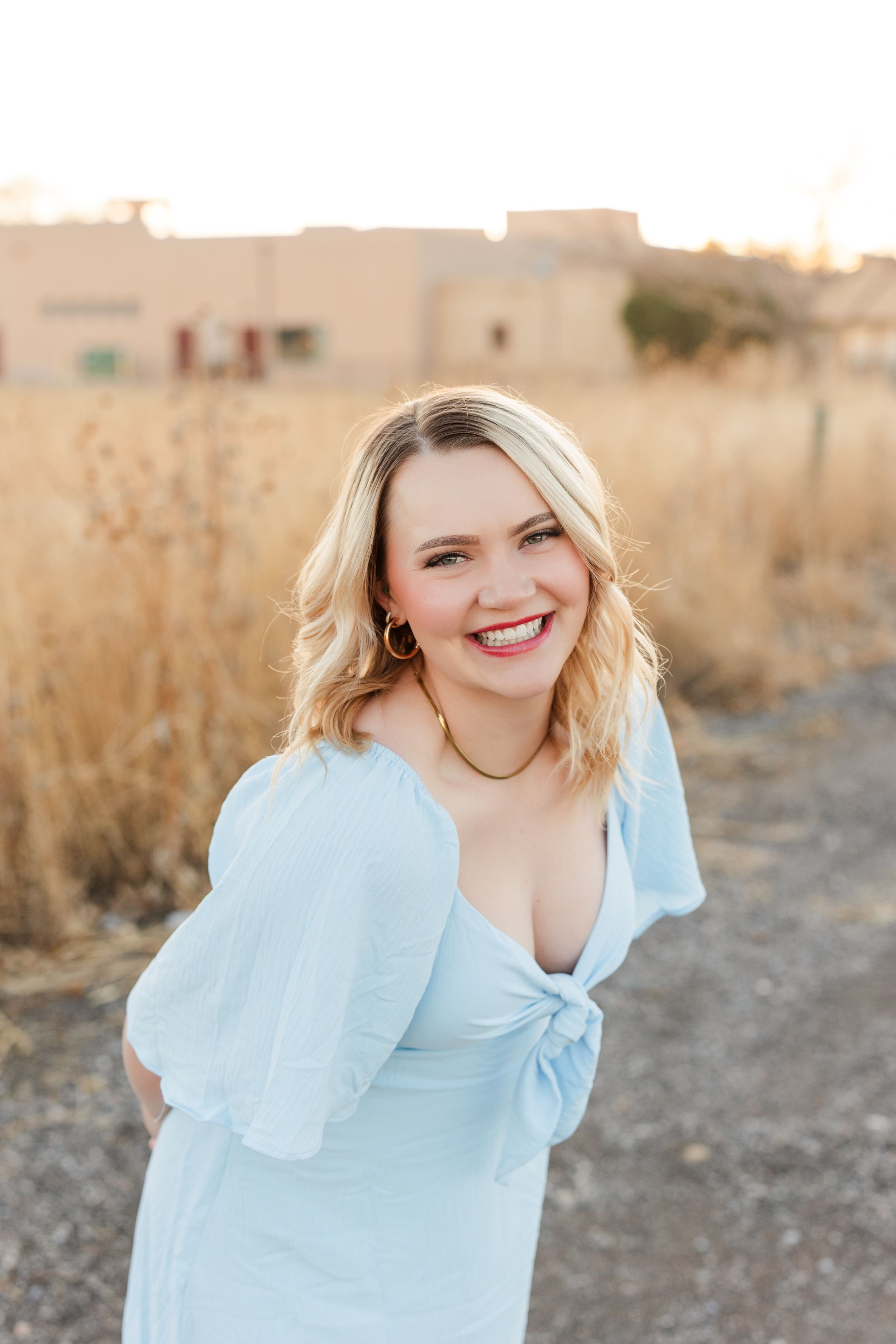 Person in a light blue dress poses outdoors in a golden field during sunset.