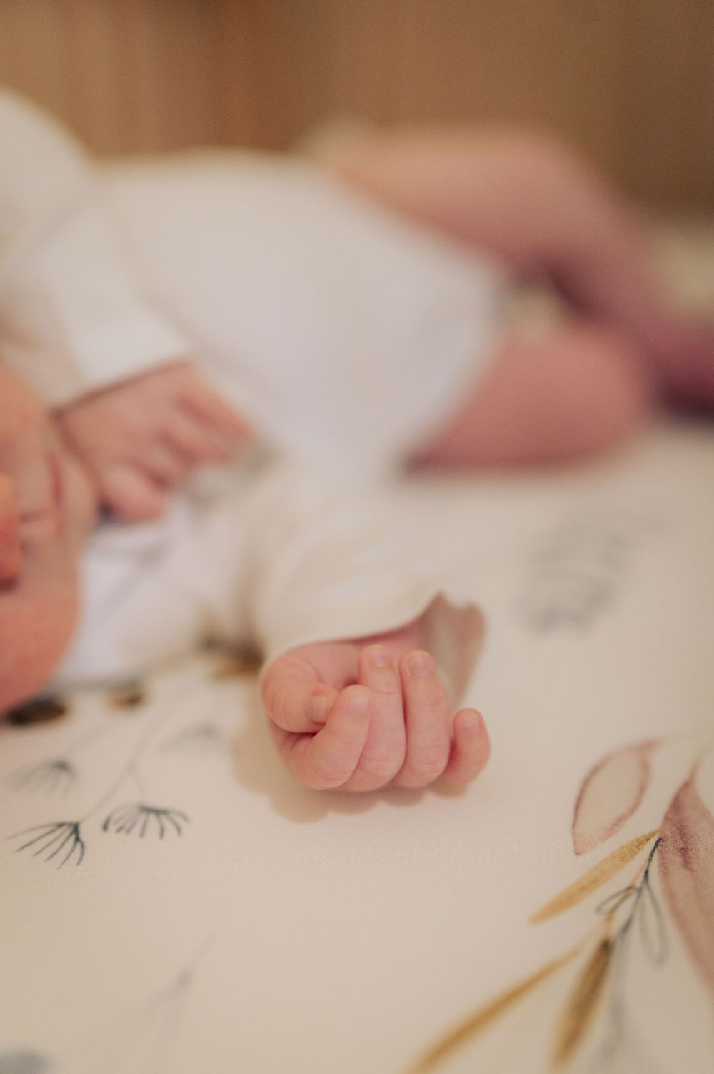 Close-up view of a tiny infant's hand resting on a floral patterned blanket.