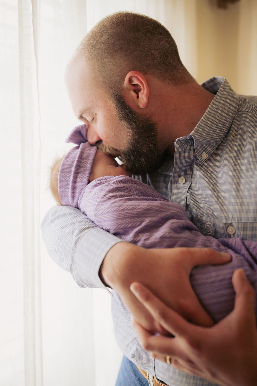 A couple in casual attire sharing an intimate embrace near a window with natural lighting.