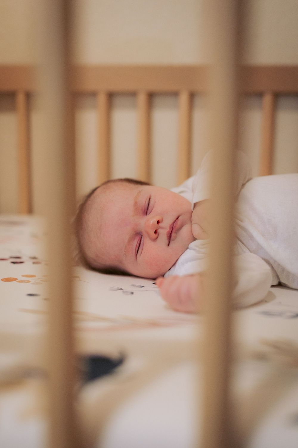 Peaceful baby sleeping soundly in a wooden crib with white bedding.