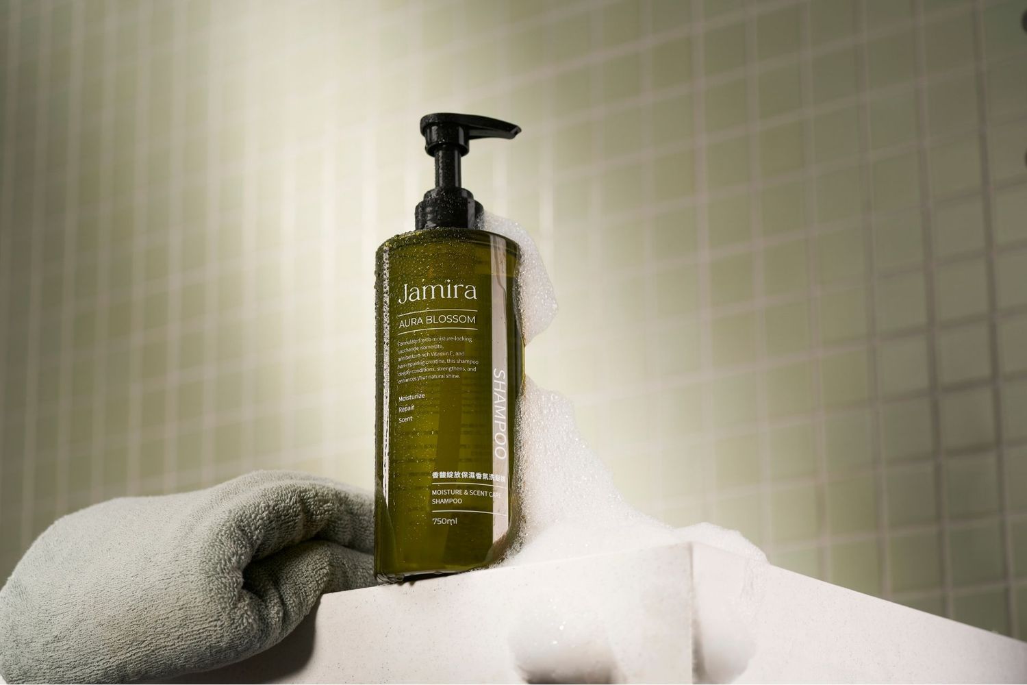 Aesmira pump bottle of green cleansing oil displayed on white towels in a modern tiled bathroom setting.