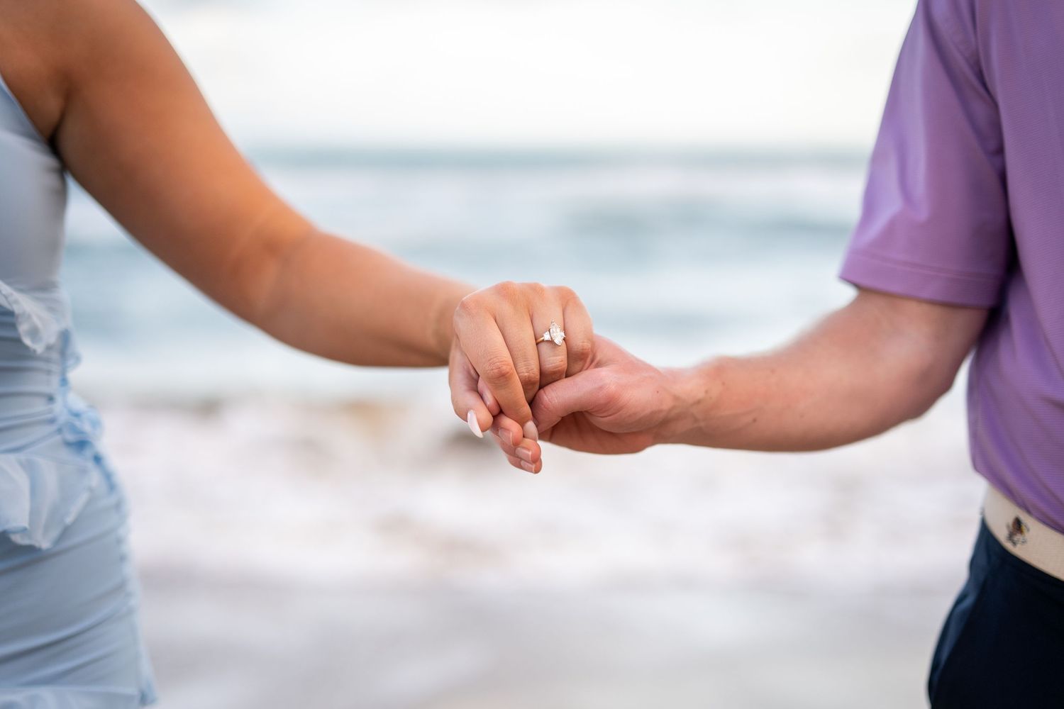 Couple embracing on rocky coastline with ocean waves in the background.
