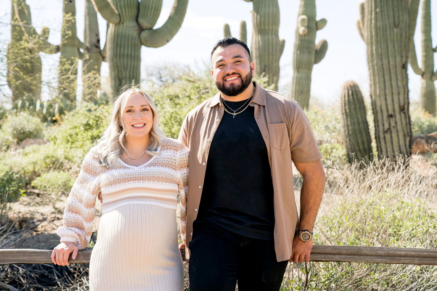 A couple poses together in the desert surrounded by tall saguaro cacti.