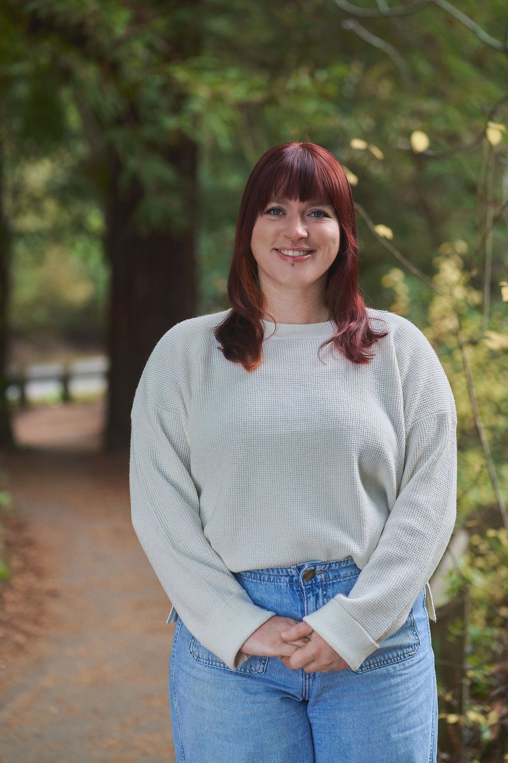 Woman with bangs wearing a light gray sweater out doors posing for professional headshots in Richmond, CA.