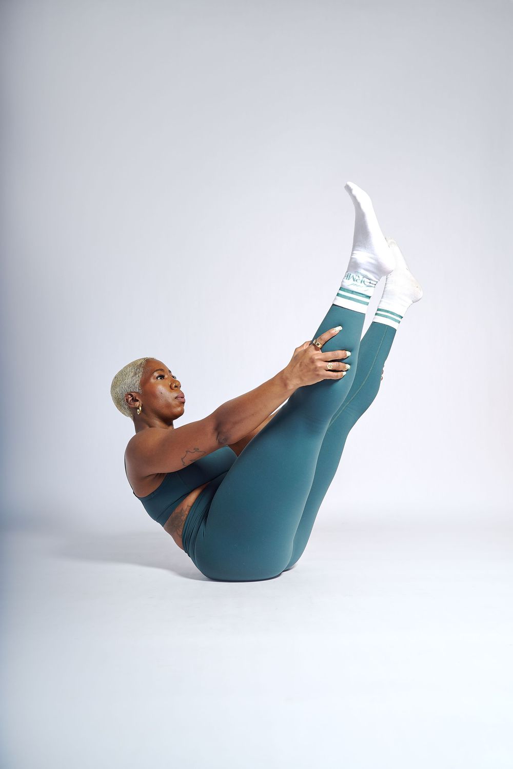 Athletic Black woman with blonde hair performing a V-sit exercise in teal leggings in an Oakland photography studio.