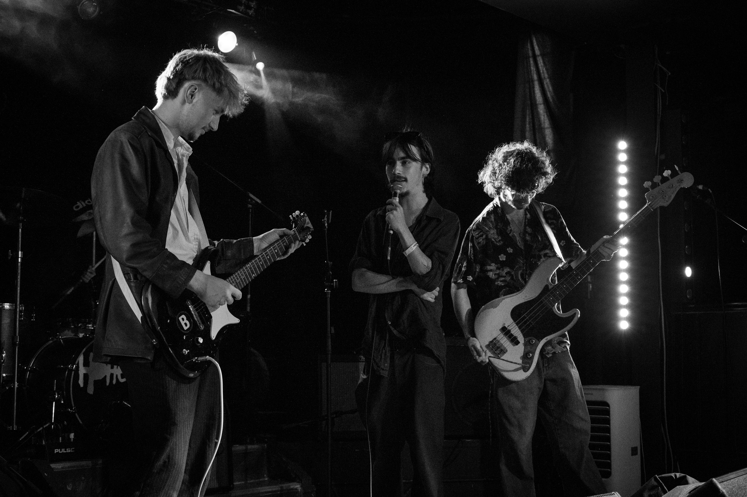 Band members perform together on stage under dramatic spotlighting in black and white.