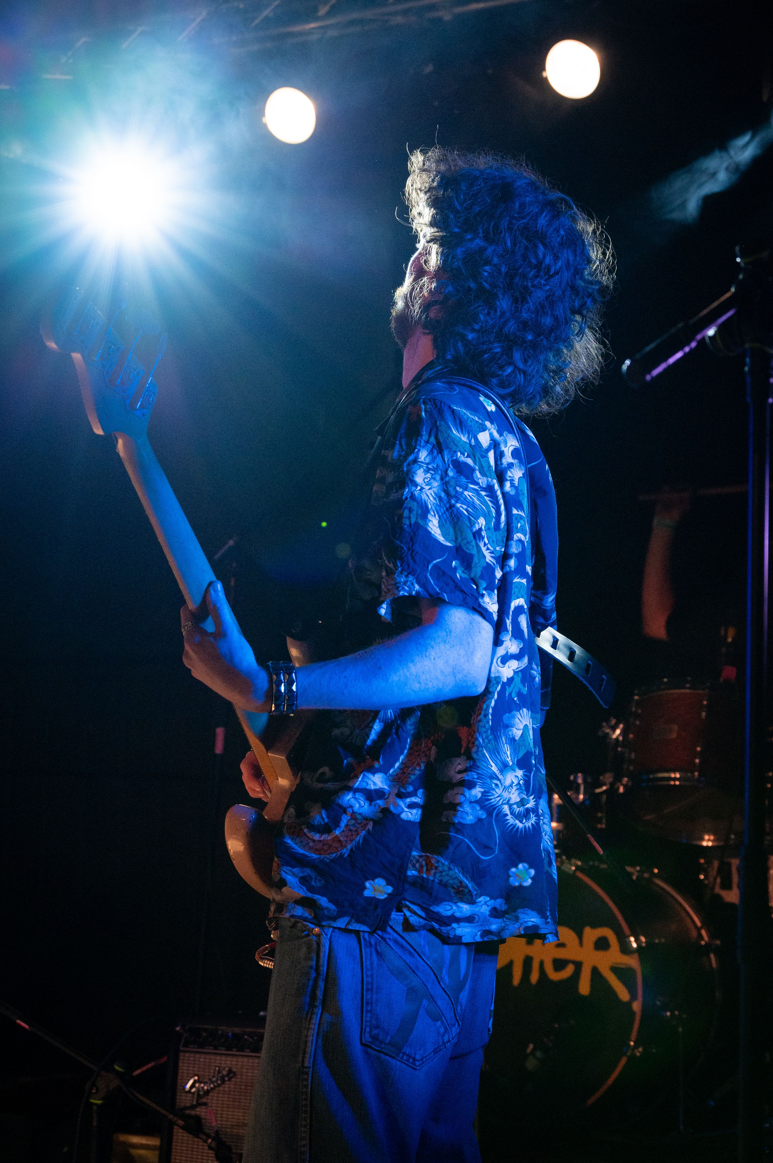 Guitarist in patterned shirt illuminated by blue stage lights during energetic performance.