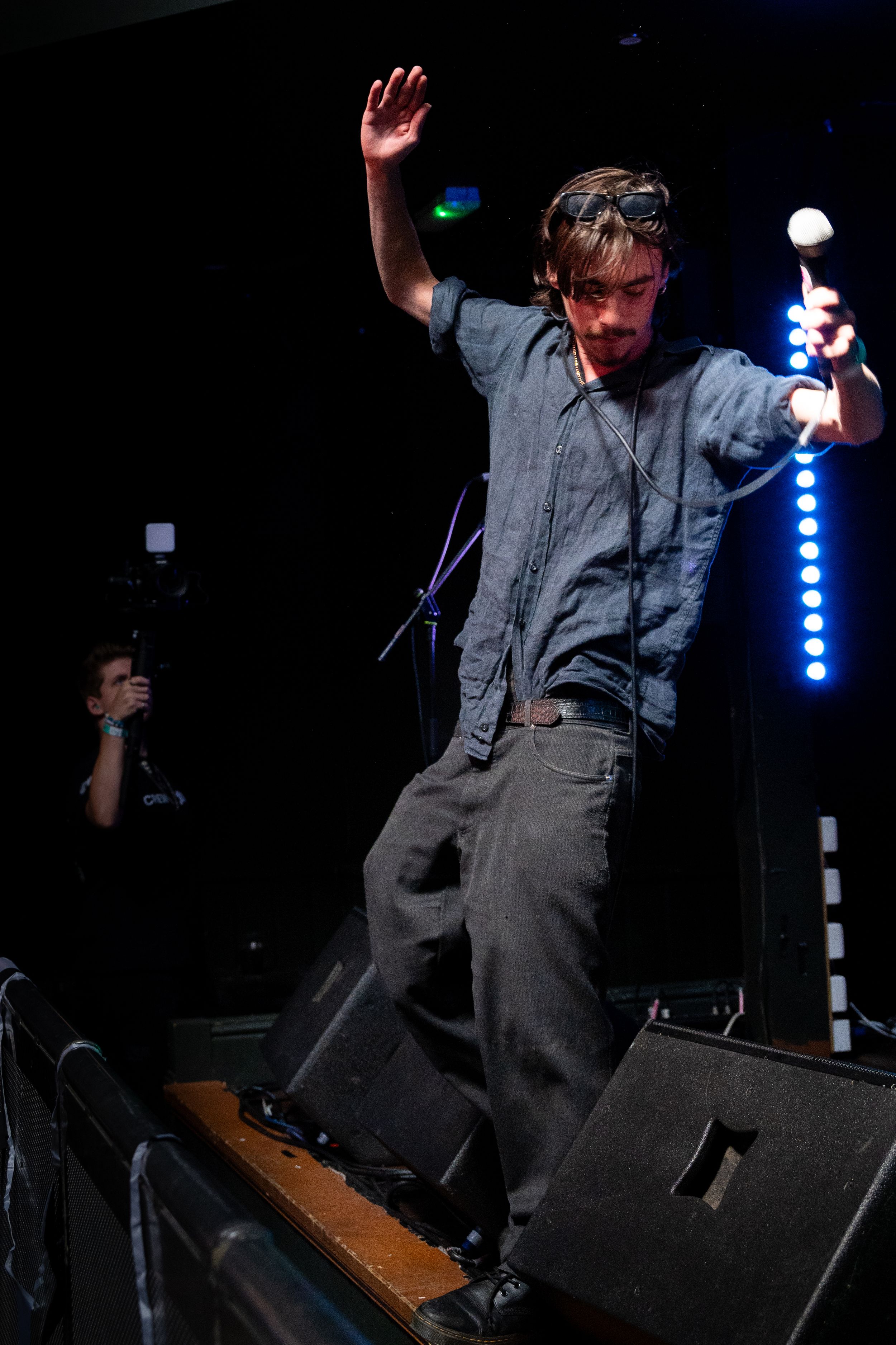 Performer raises arm while standing energetically on stage equipment during concert.