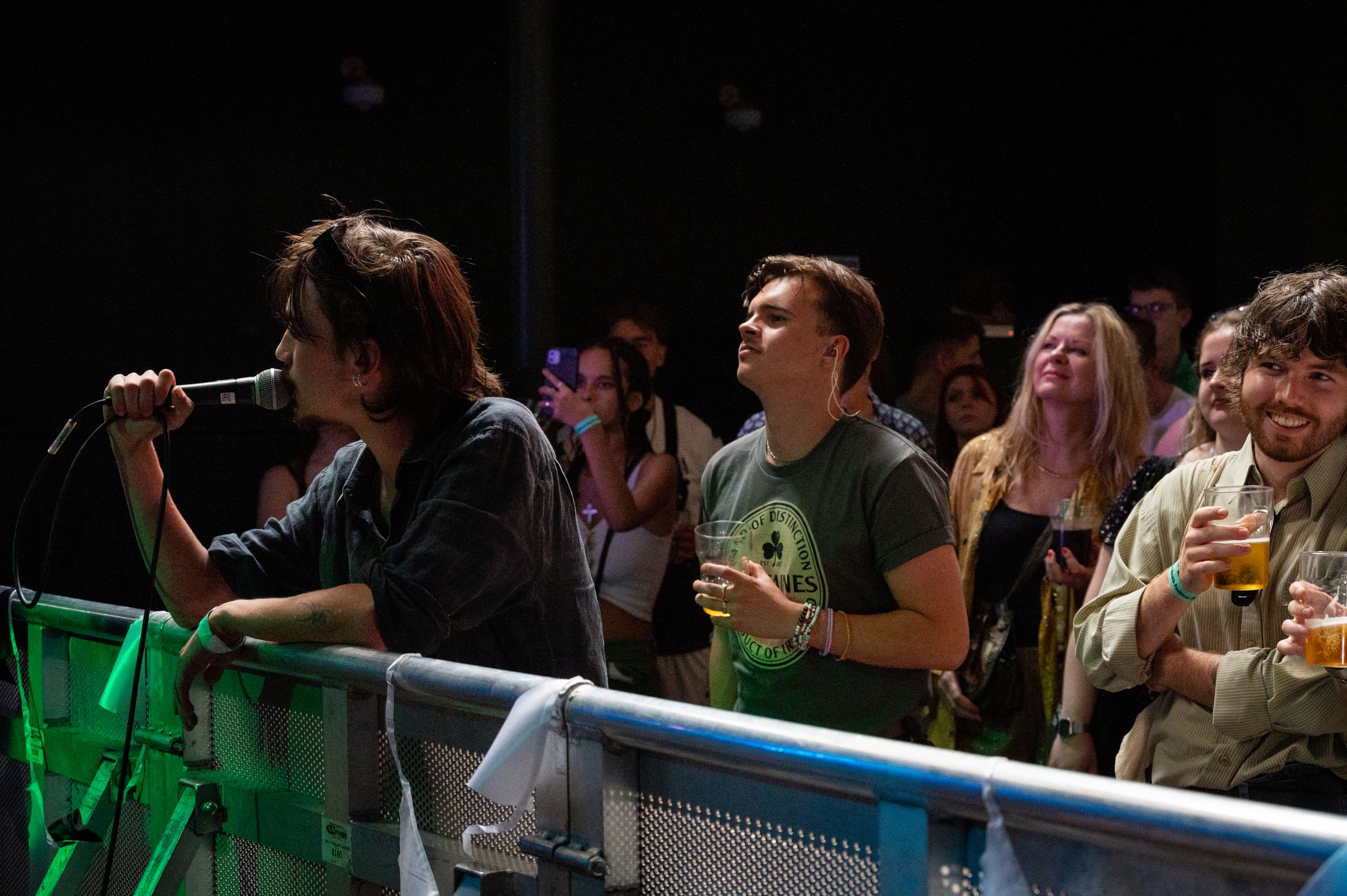 Concert audience members enjoy the show from behind a barricade in green lighting.
