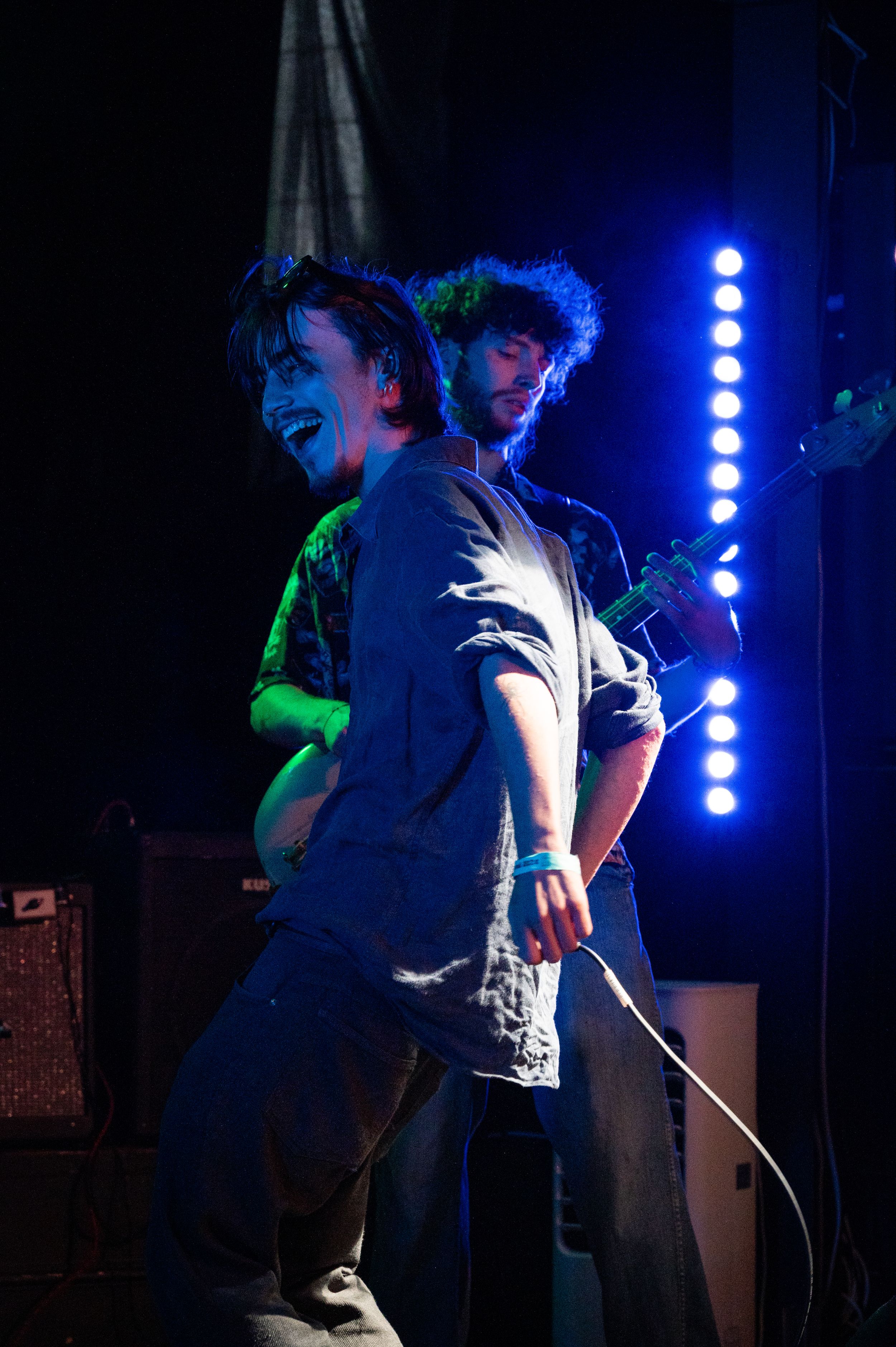 Musicians performing energetically on stage with dramatic blue backlighting.