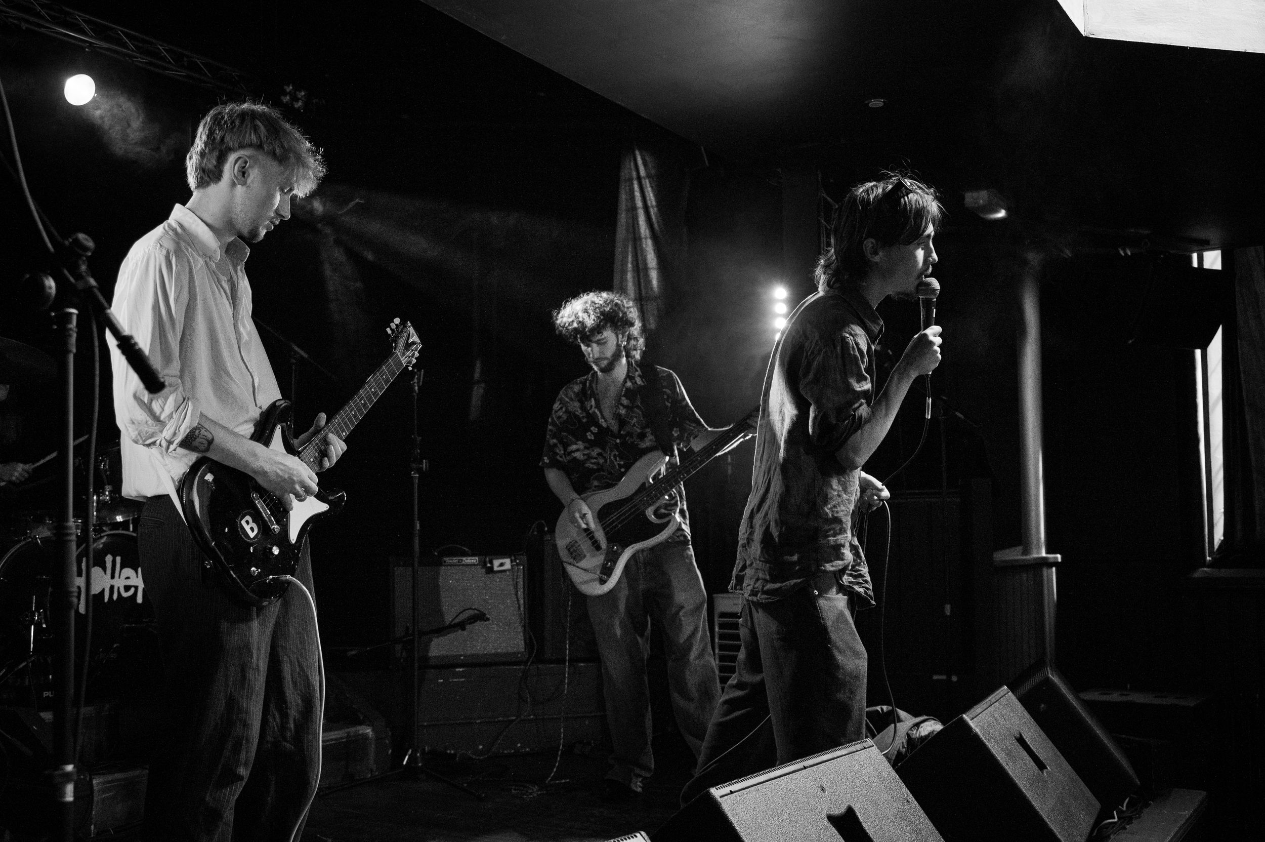 Black and white photo of band members performing with instruments on dark stage.