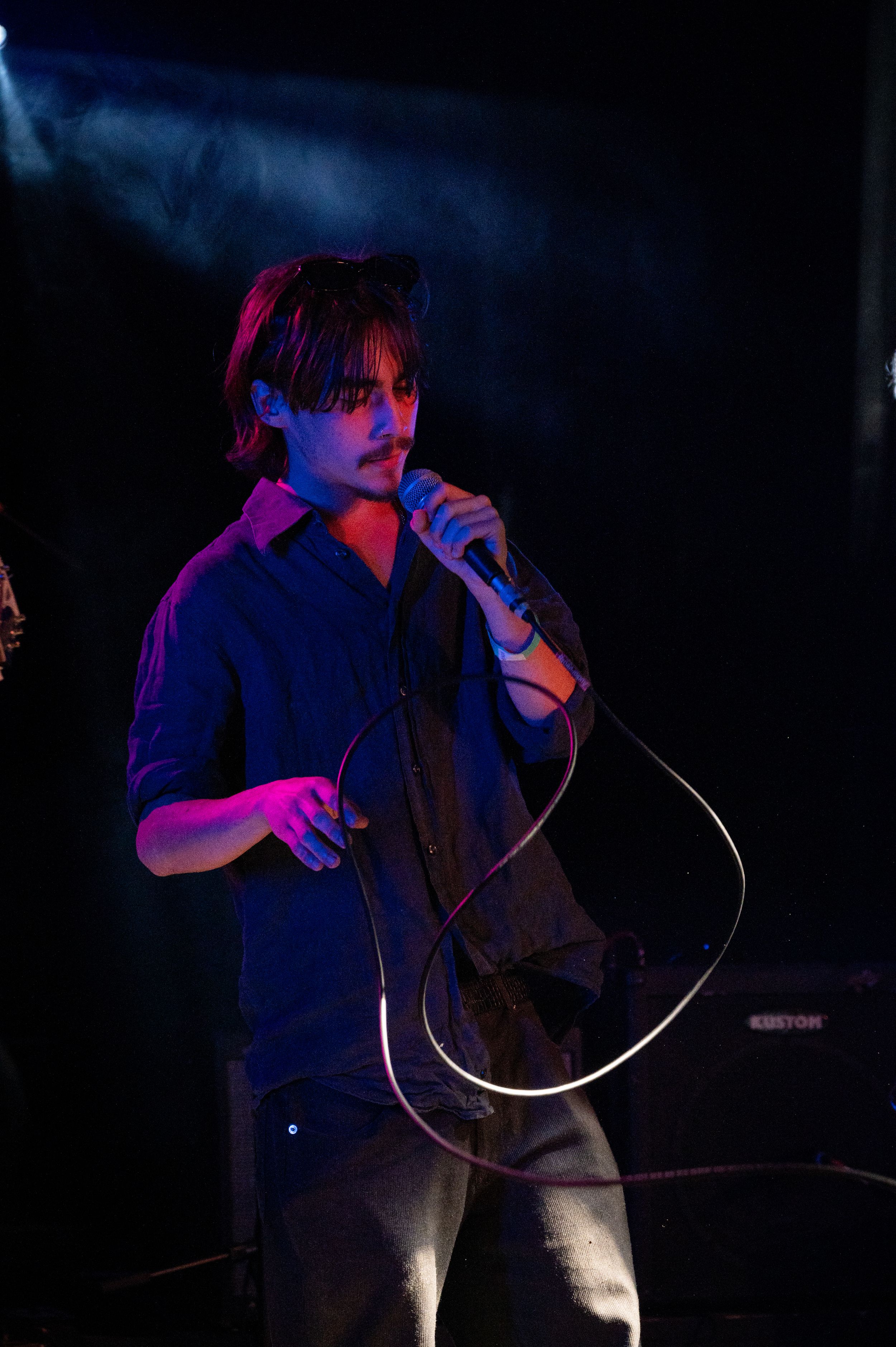 Singer performs with microphone under purple stage lighting at concert venue.