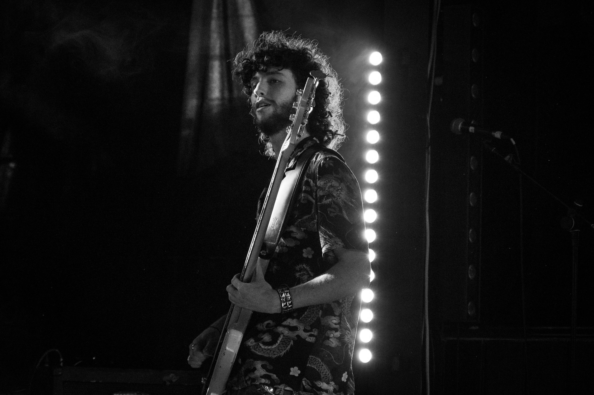 Black and white portrait of guitarist performing with vertical light strip in background.
