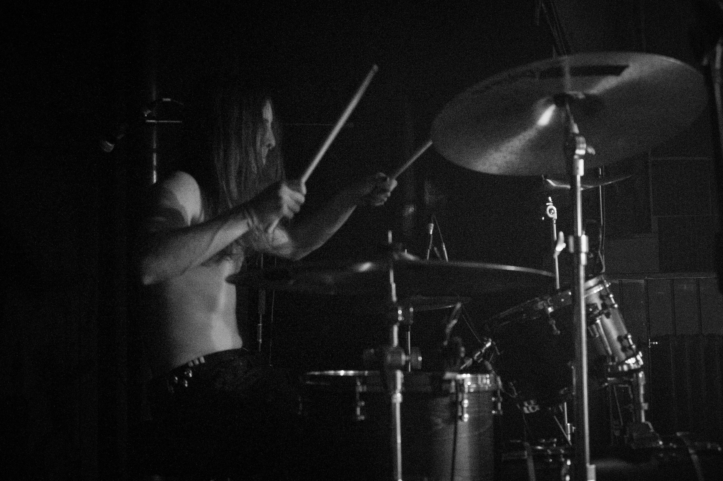 Drummer performs energetically on stage in dramatic black and white lighting.