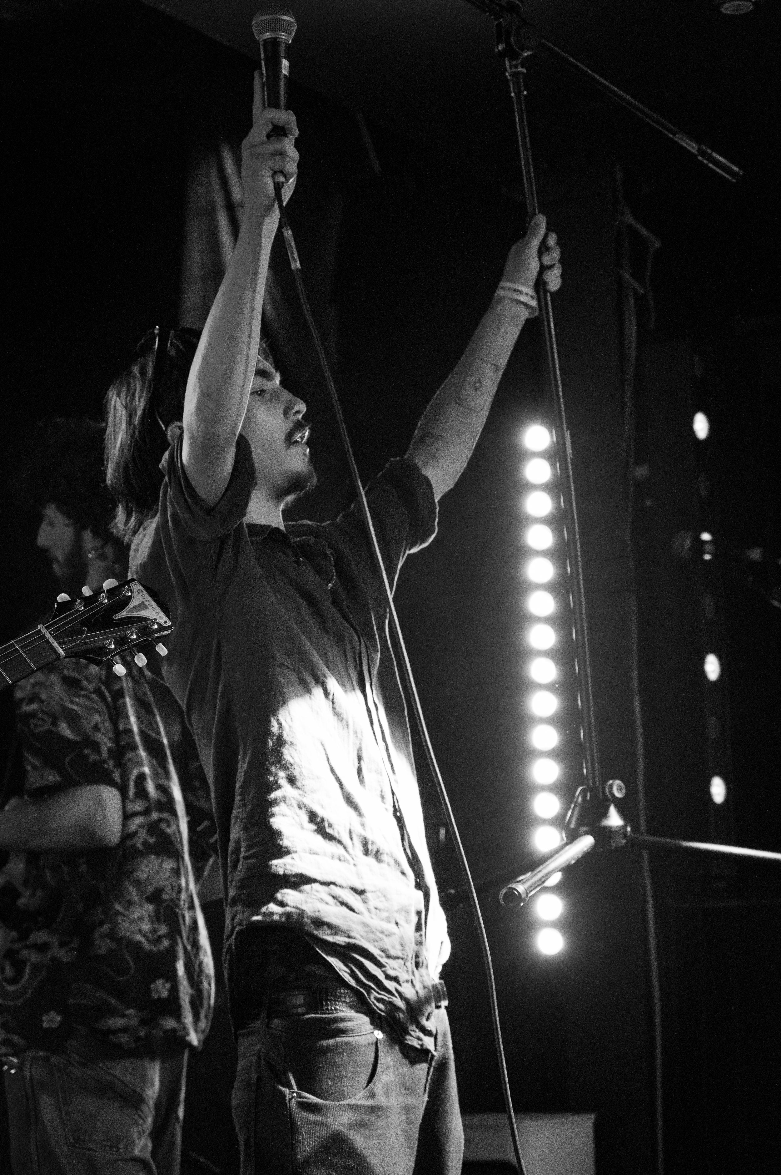 Concert performer raises microphone stand during energetic black and white performance shot.