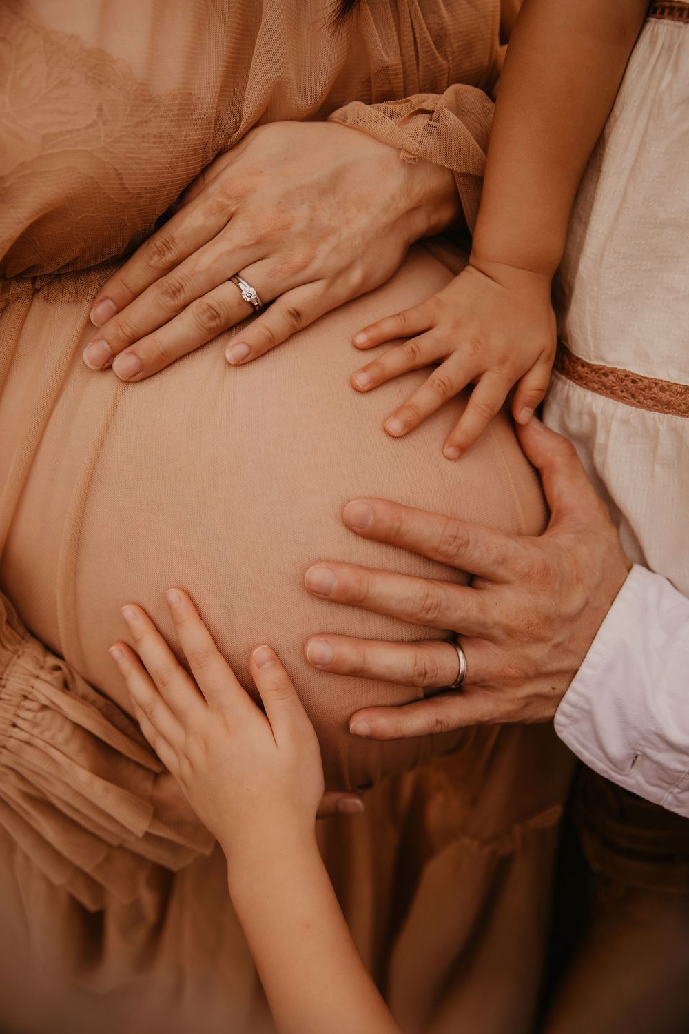 Family hands tenderly cradling a pregnant belly, with wedding rings visible, capturing a beautiful maternity moment.