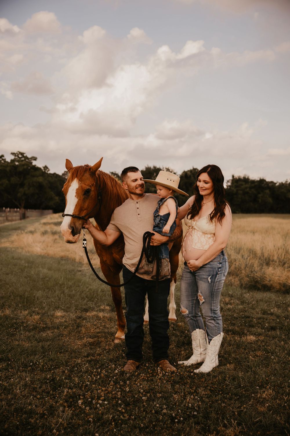 A couple in a field with their brown horse during a golden hour outdoor photoshoot.