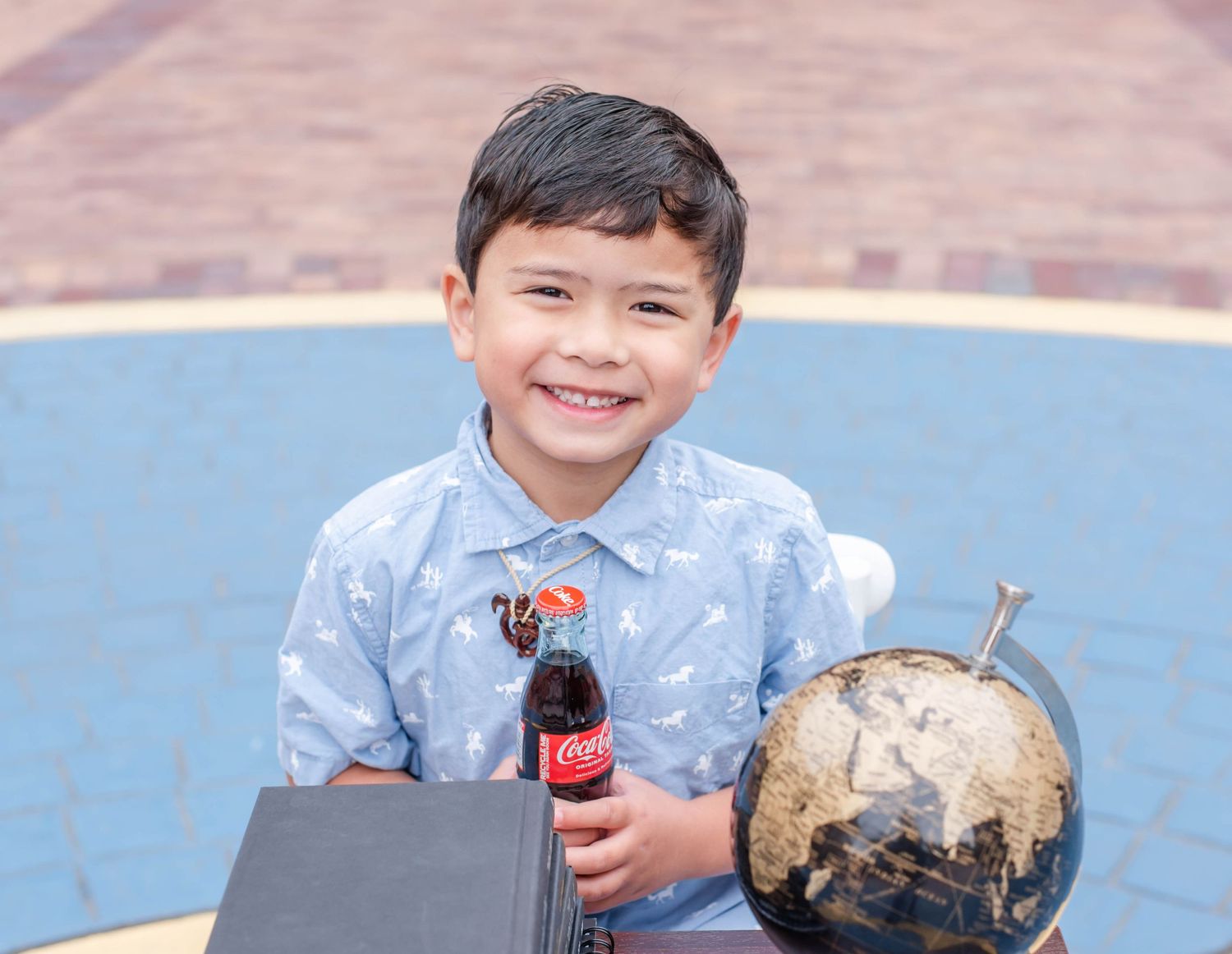 Child sits at outdoor table with stack of books and Coca-Cola for reading break.