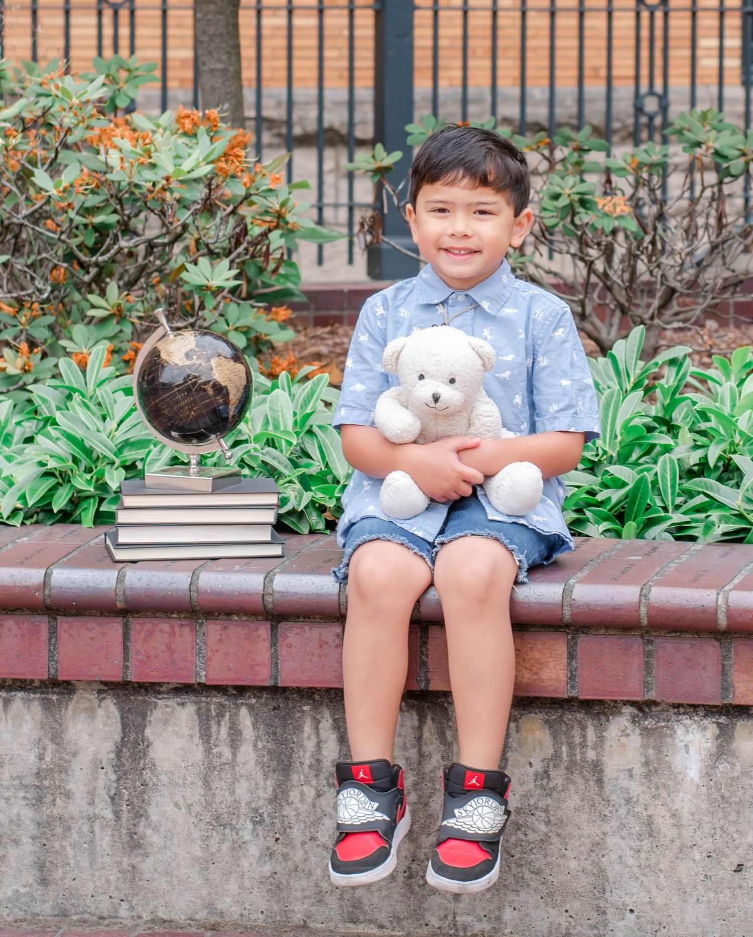 Child in blue shirt sits on brick ledge with stuffed animal toy outdoors.