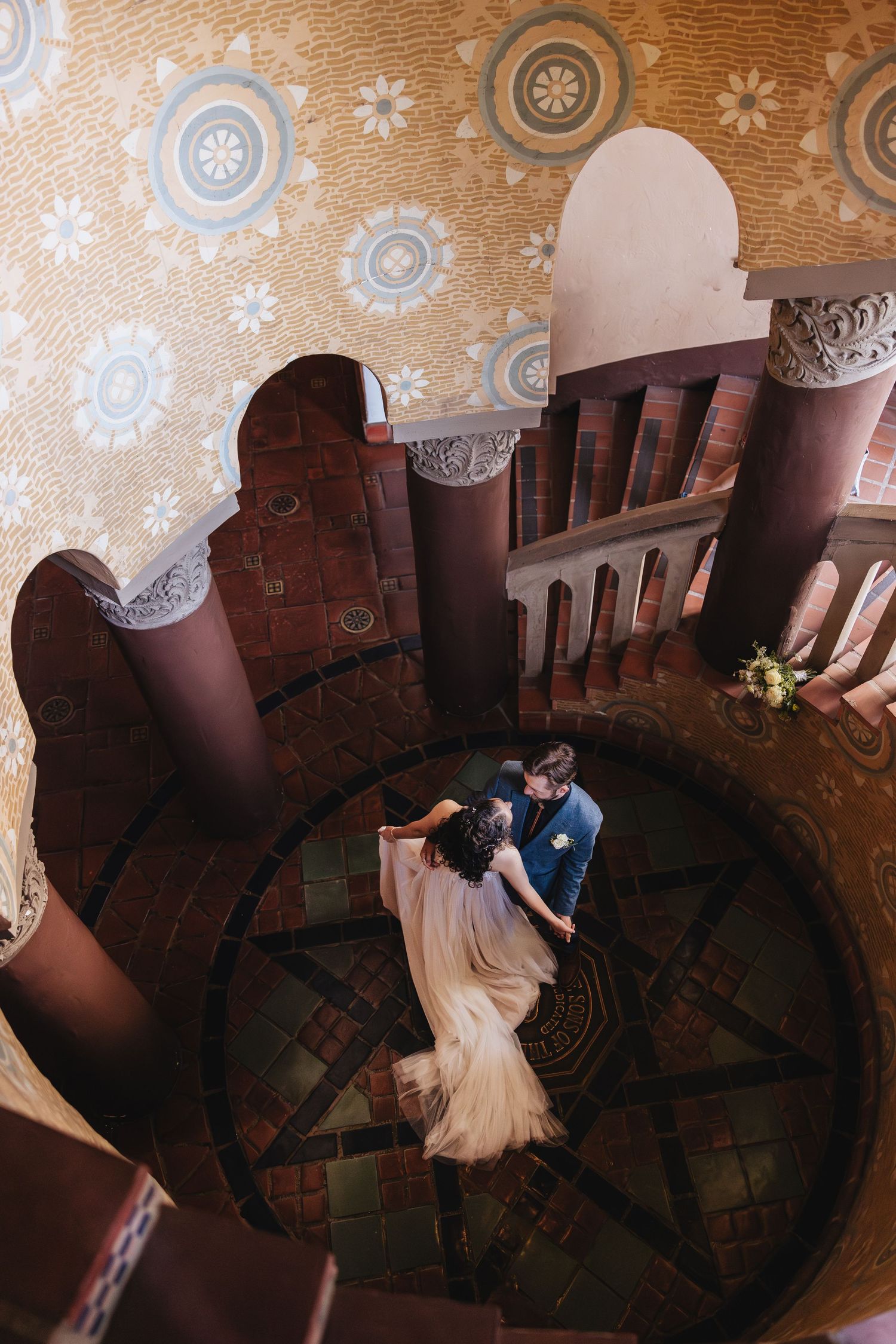 Aerial view of a couple dancing in an ornate circular room with vintage wallpaper and decorative moldings.