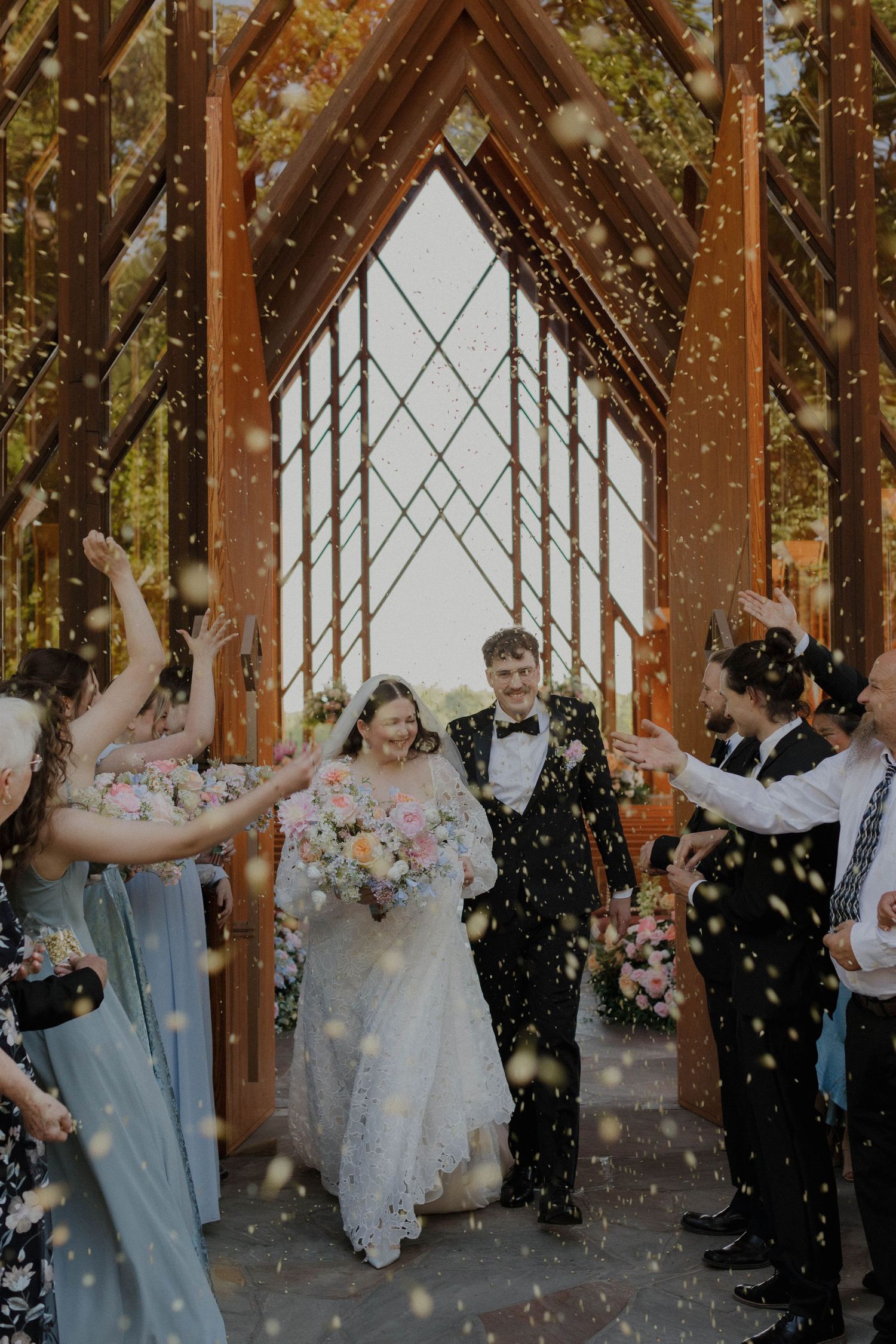 Wedding celebration with confetti shower under wooden beams decorated with fairy lights.