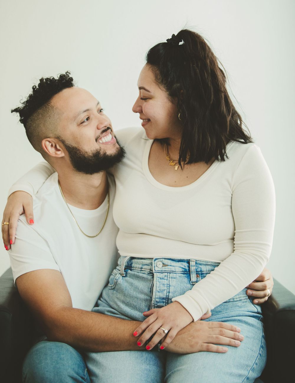 A couple in casual attire shares intimate moments against a white background during a photo session.