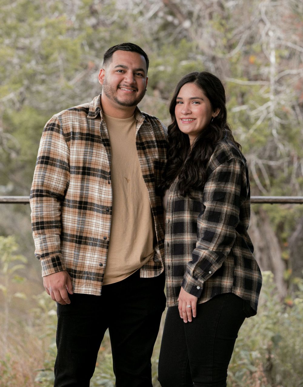 Couple in plaid and casual wear posing together in natural outdoor setting.
