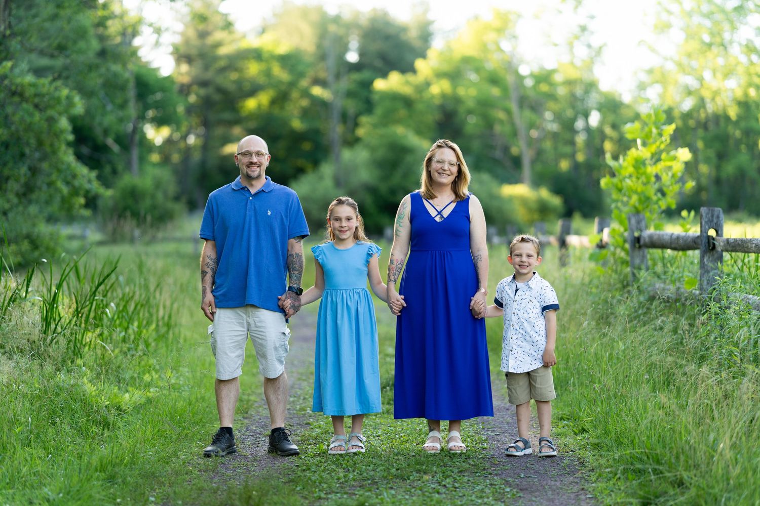 Family of four standing together on outdoor path surrounded by greenery.