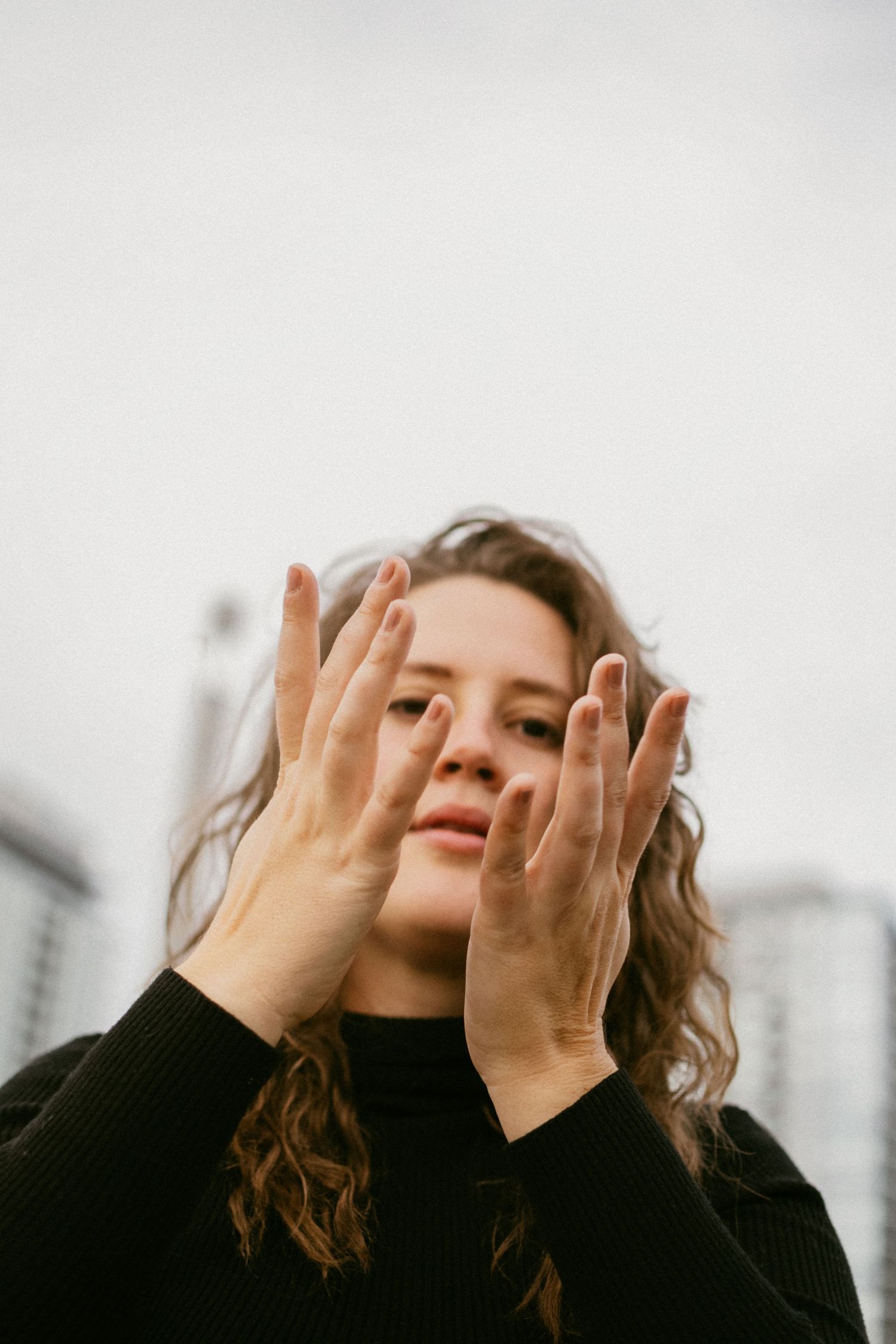 Emotional portrait of someone covering their face with both hands against a city backdrop.
