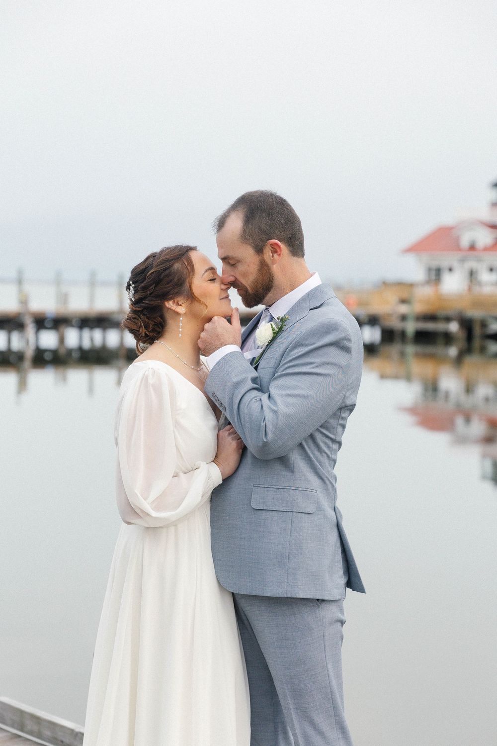 Wedding couple sharing romantic moments on a coastal dock with calm waters in background.